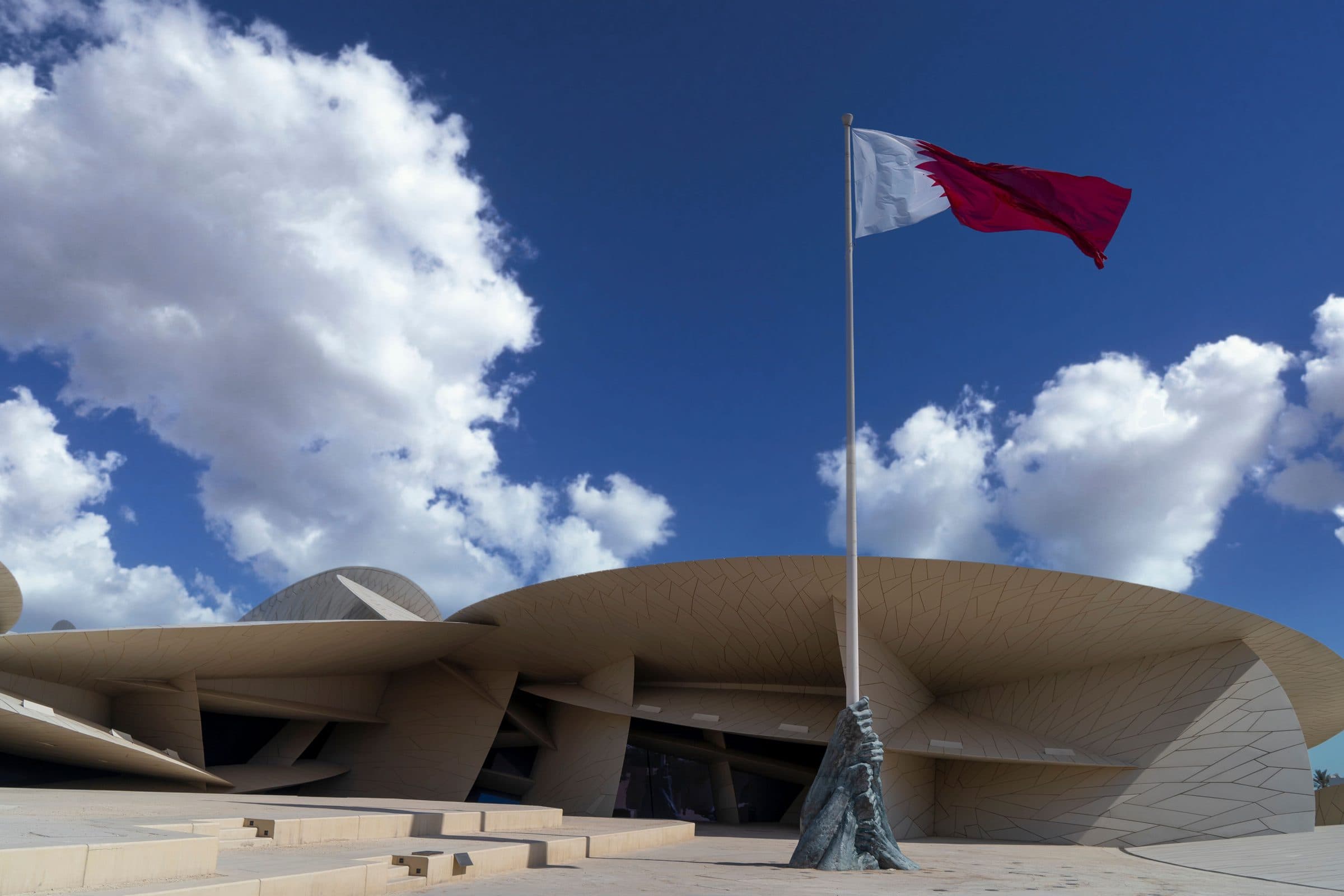Museu Nacional do Catar e bandeira sob o céu azul com nuvens em Doha