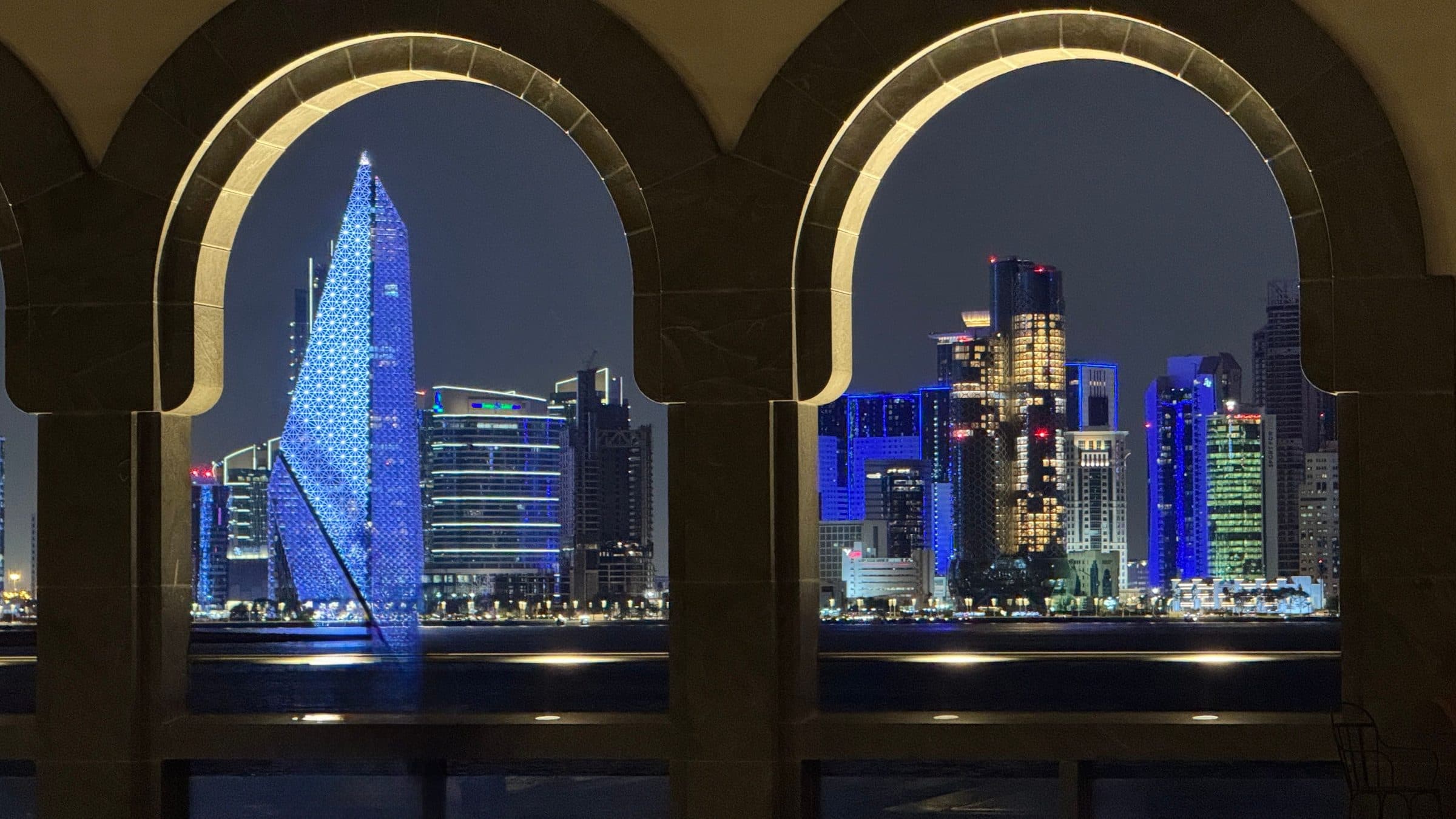 Vista noturna dos arranha-céus iluminados de Doha através de arcos decorativos