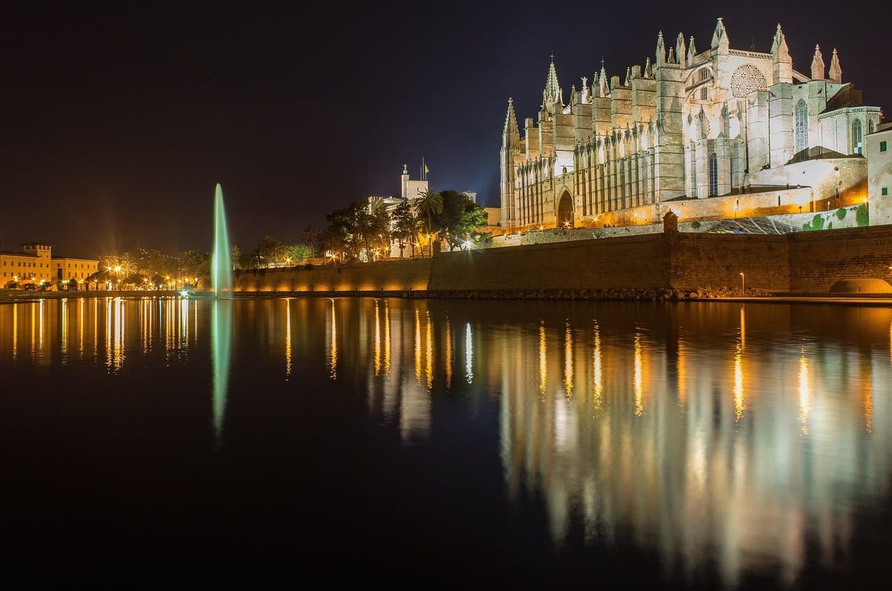 Catedral de Palma de Mallorca iluminada à noite com reflexos na água