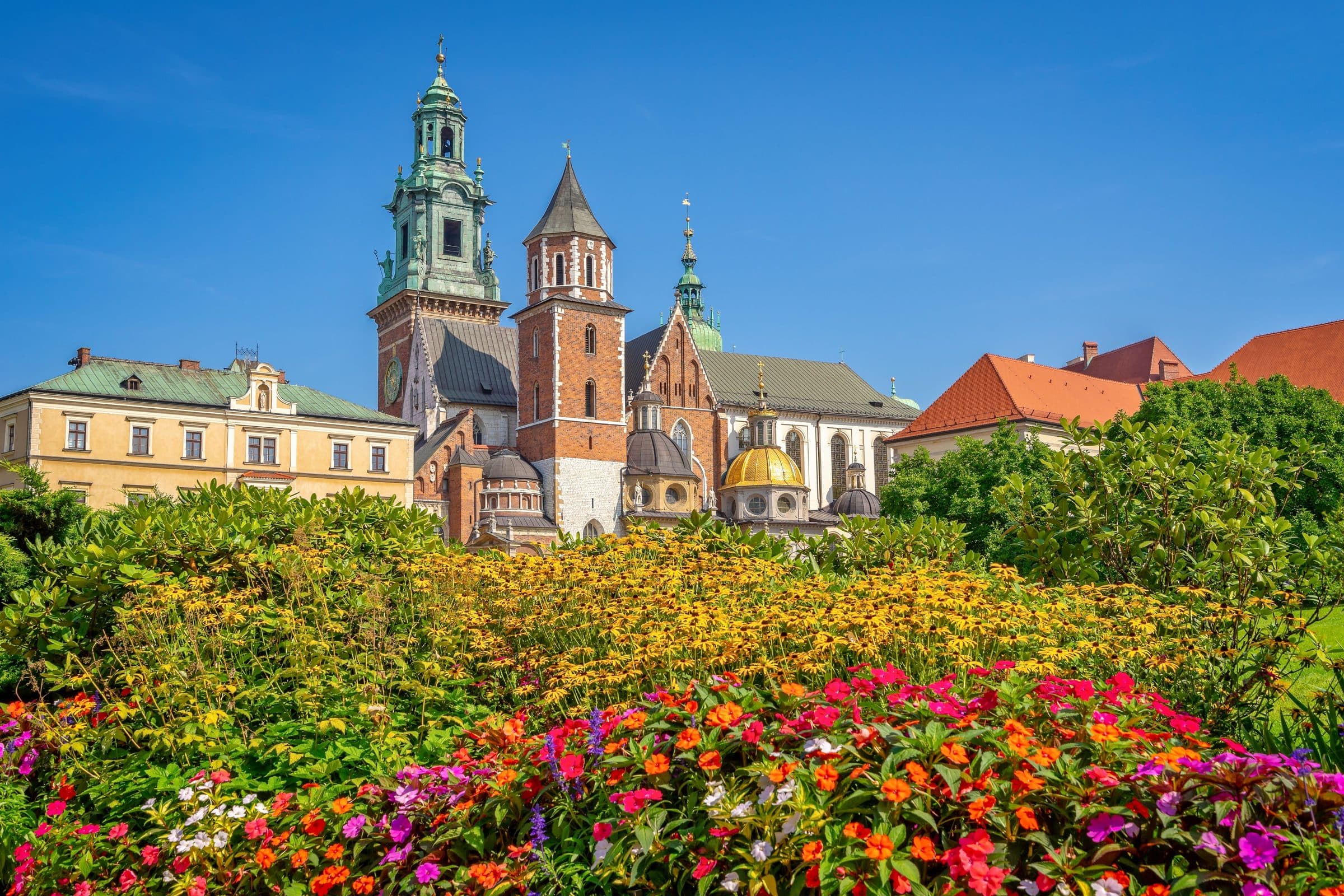 Vista da Catedral de Wawel em Cracóvia com flores coloridas em primeiro plano e céu azul