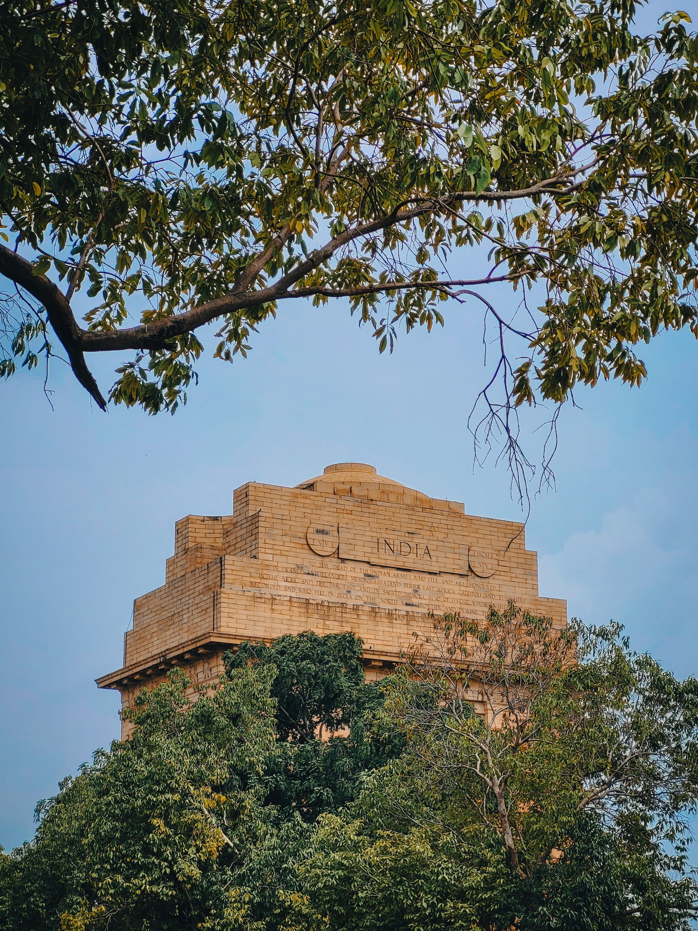 O monumento India Gate em New Delhi em dia ensolarado, cercado por árvores sob céu azul
