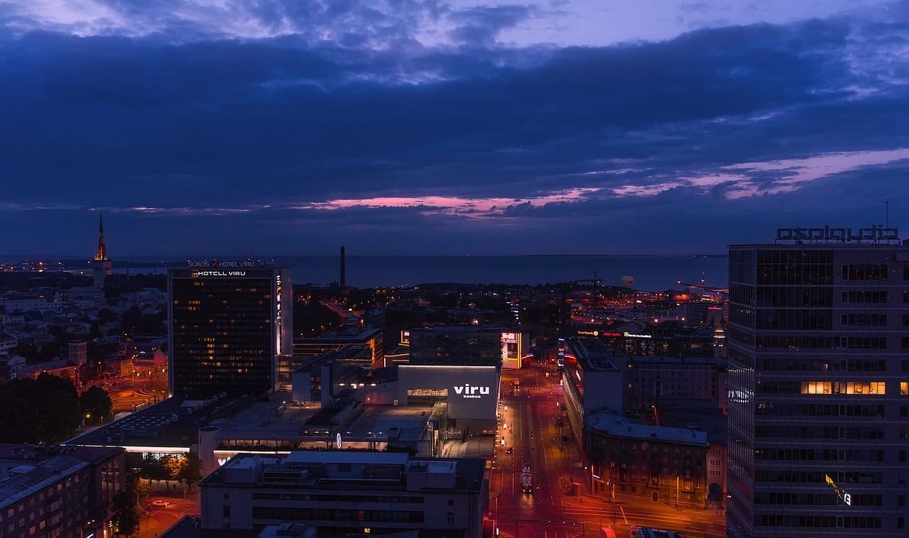 Panorama urbano de Tallinn ao entardecer com vista para o mar e prédios iluminados