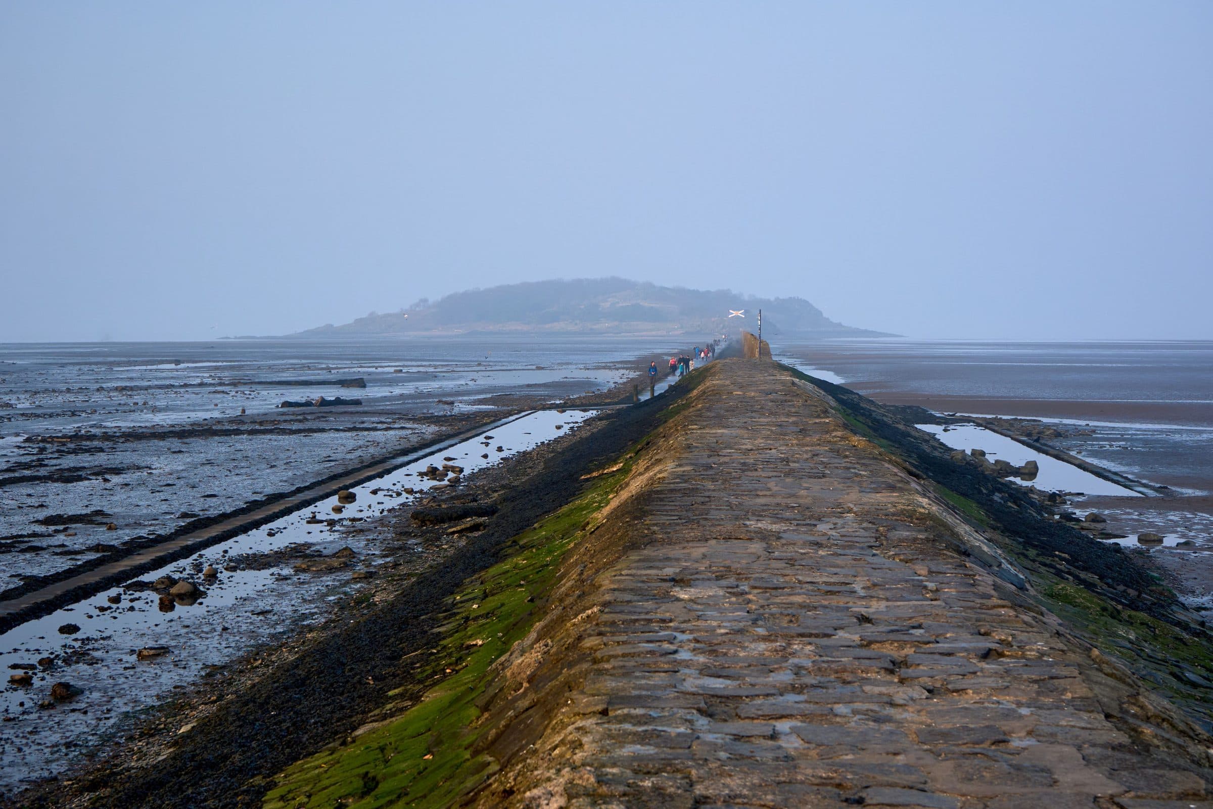 Pessoas caminham por calçada de pedra na maré baixa em direção a Cramond Island, na Escócia