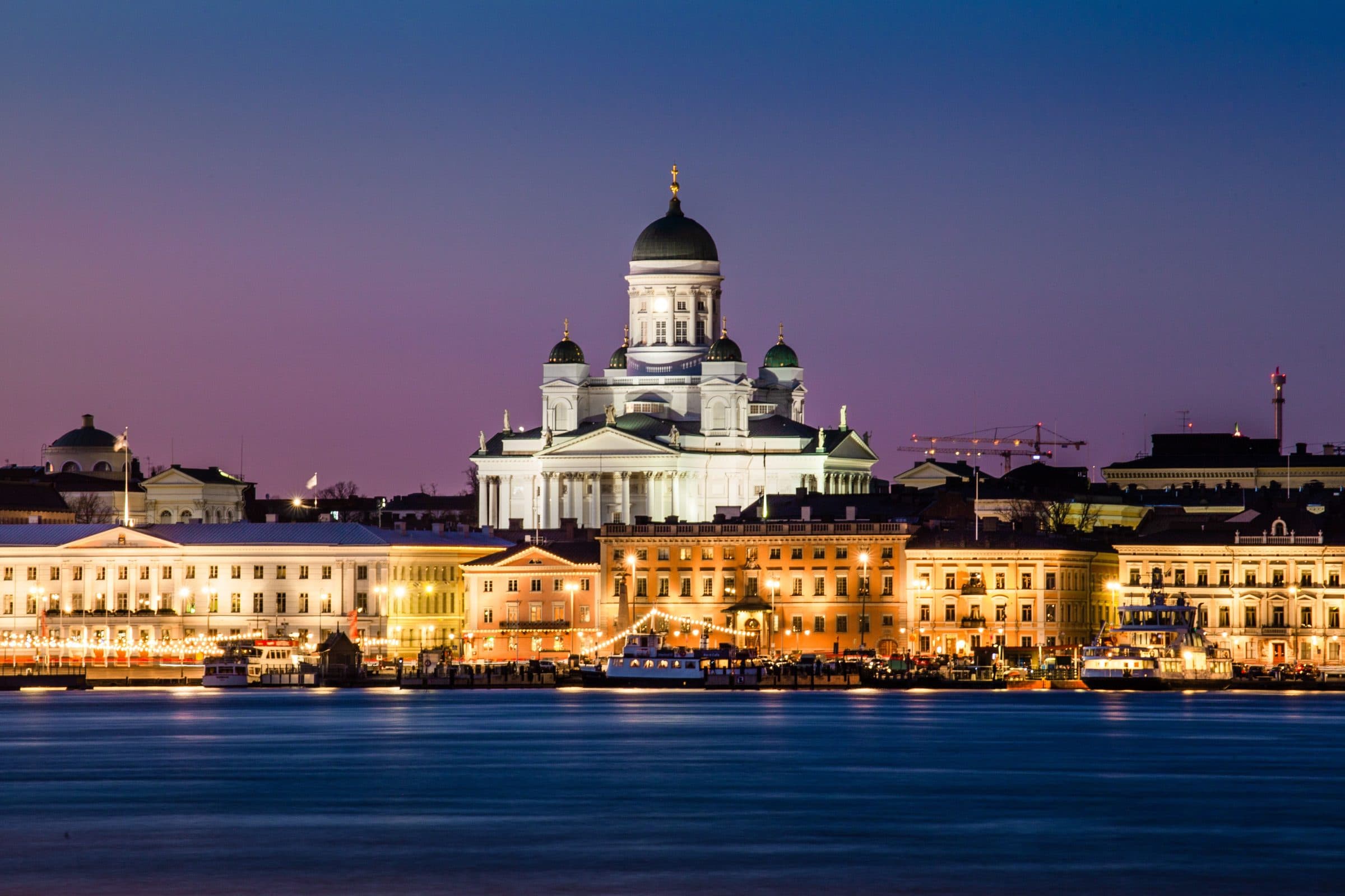 Catedral de Helsinque iluminada ao entardecer com reflexos na água