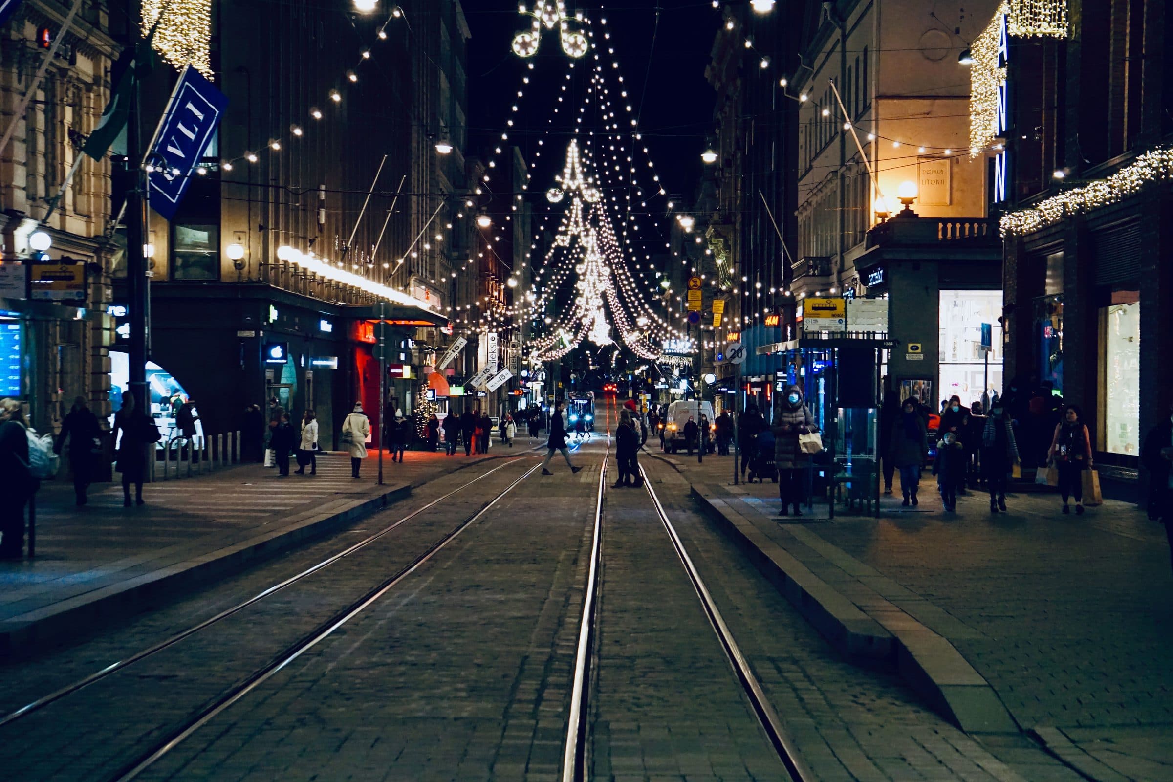 Centro de Helsinque à noite com iluminação de Natal, pedestres e bondes circulando