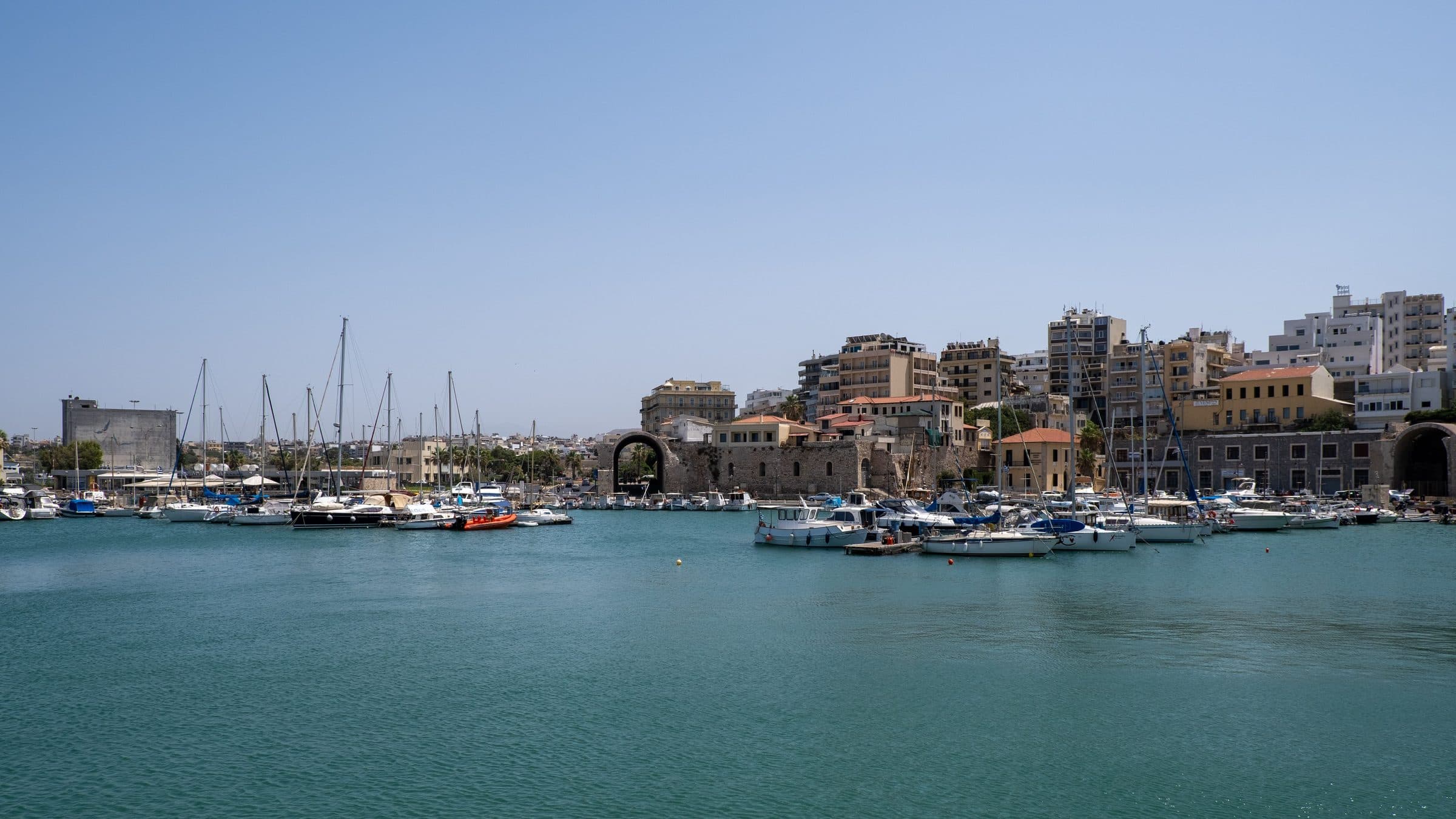 Porto de Heraklion com veleiros e paisagem urbana sob o céu azul