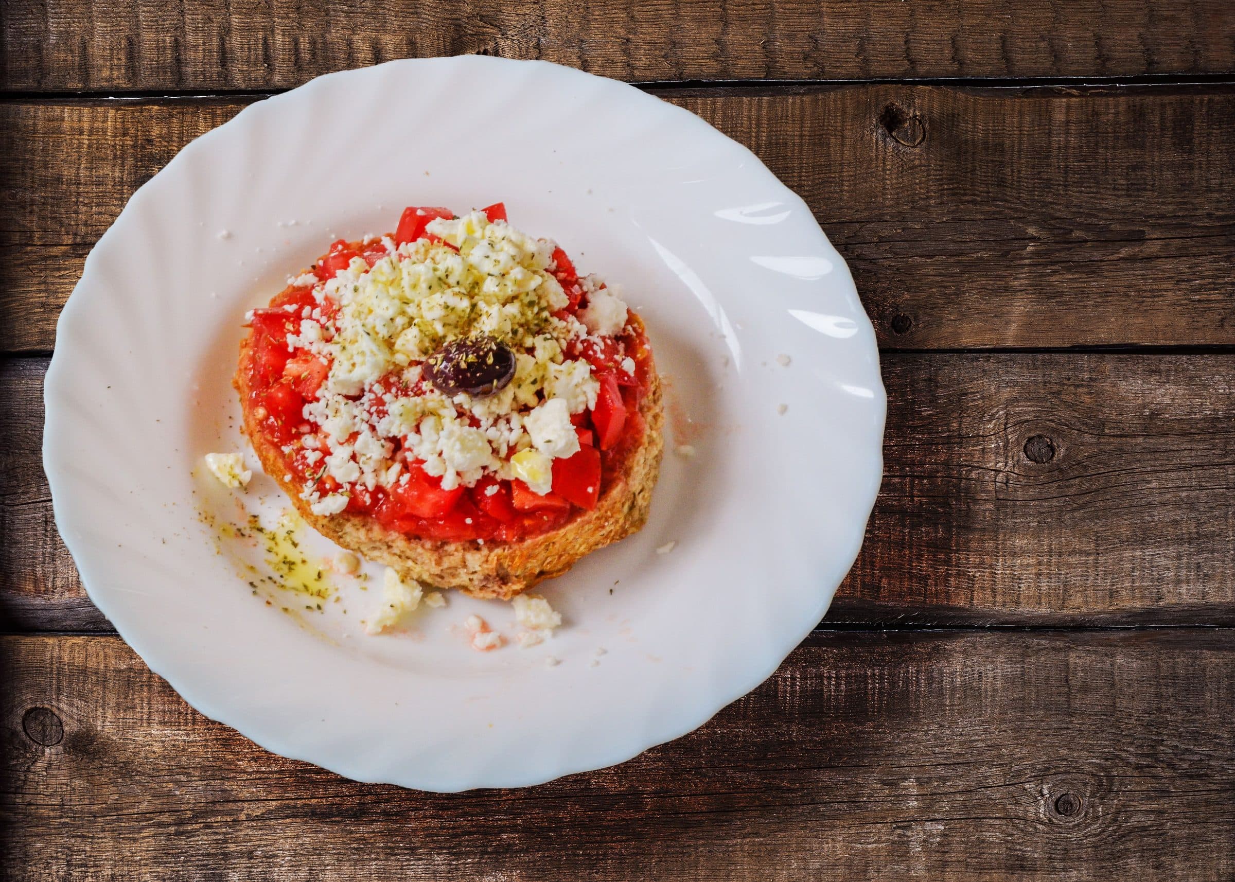 Salada dakos com queijo feta, tomate e azeitonas servida sobre uma mesa de madeira