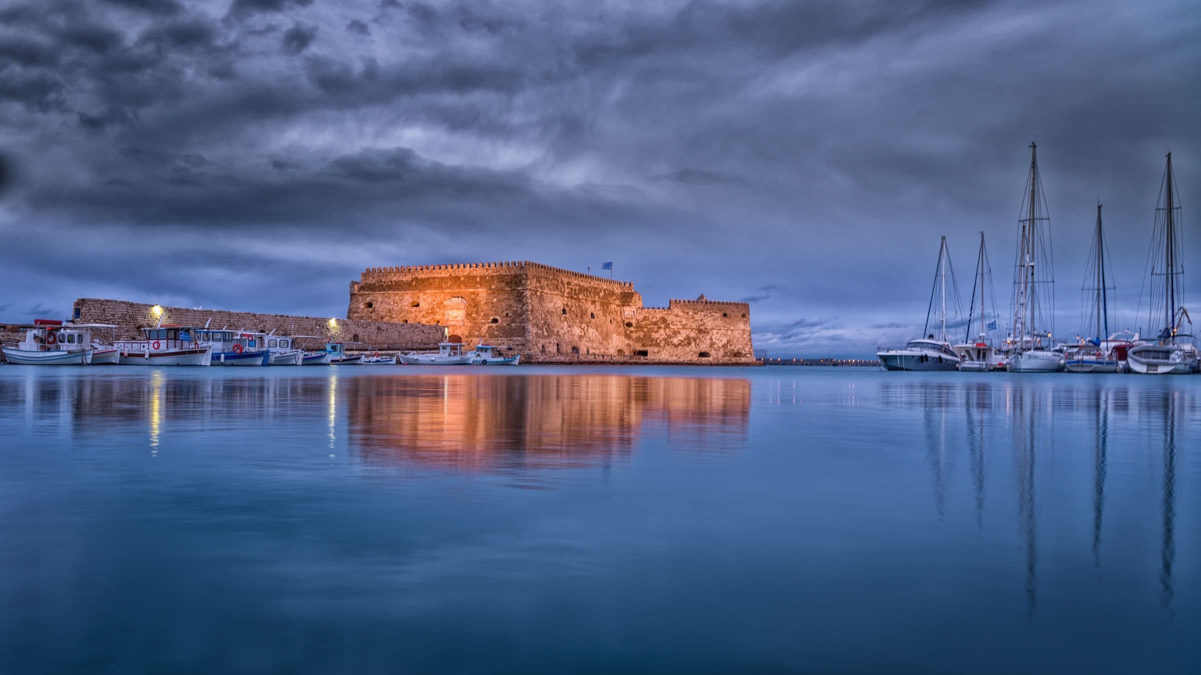 Fortaleza de Koules refletida nas águas calmas do porto de Heraklion ao entardecer