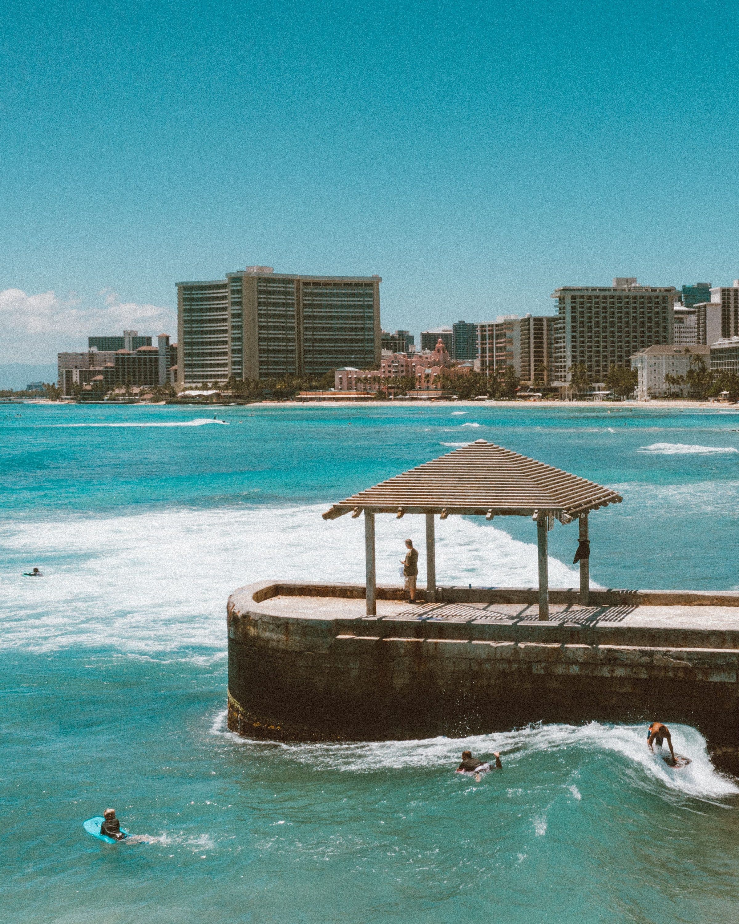 Surfistas no mar da praia de Waikiki com os prédios de Honolulu ao fundo