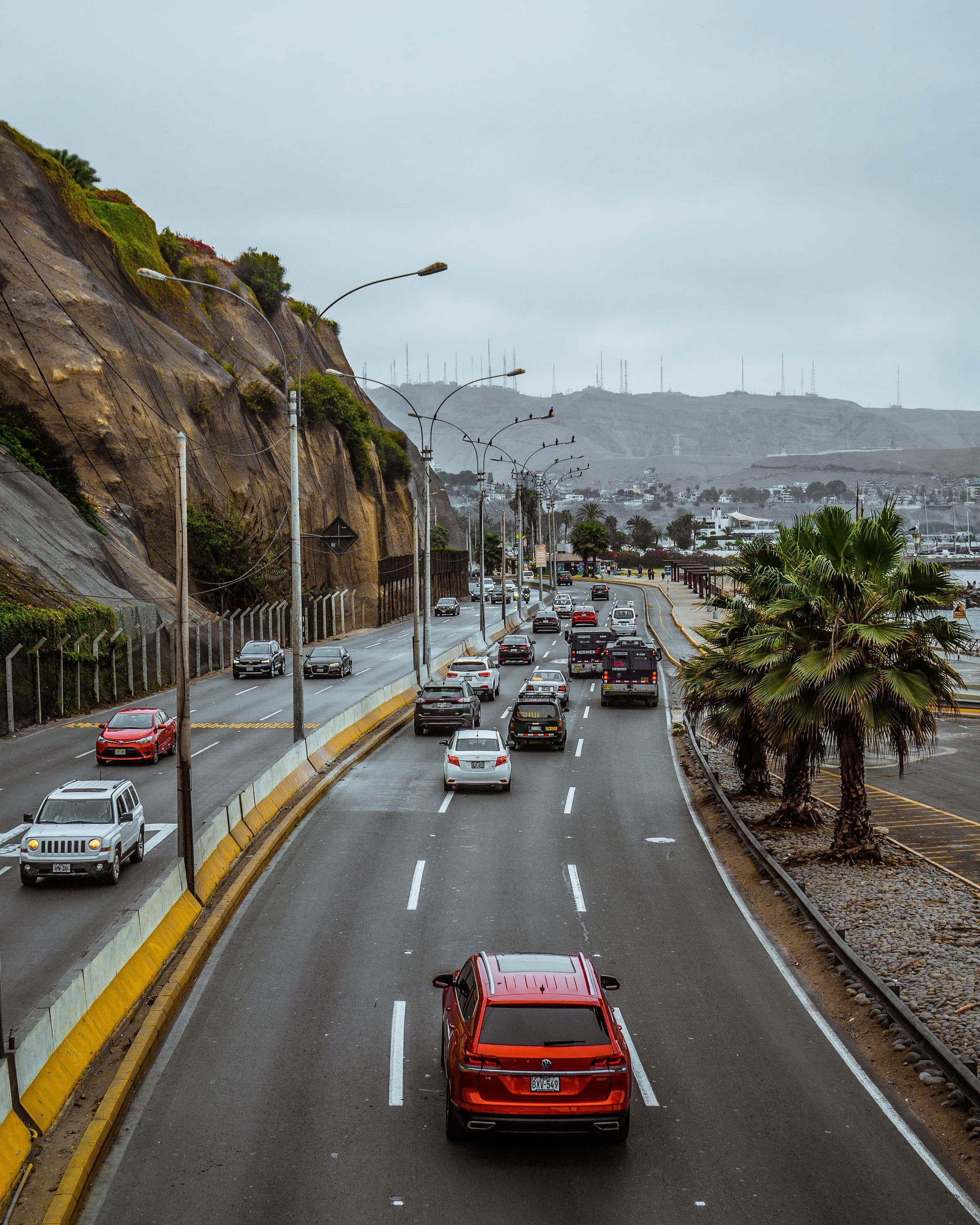 Trânsito movimentado em estrada costeira com vista para falésias e paisagem urbana em Lima, Peru