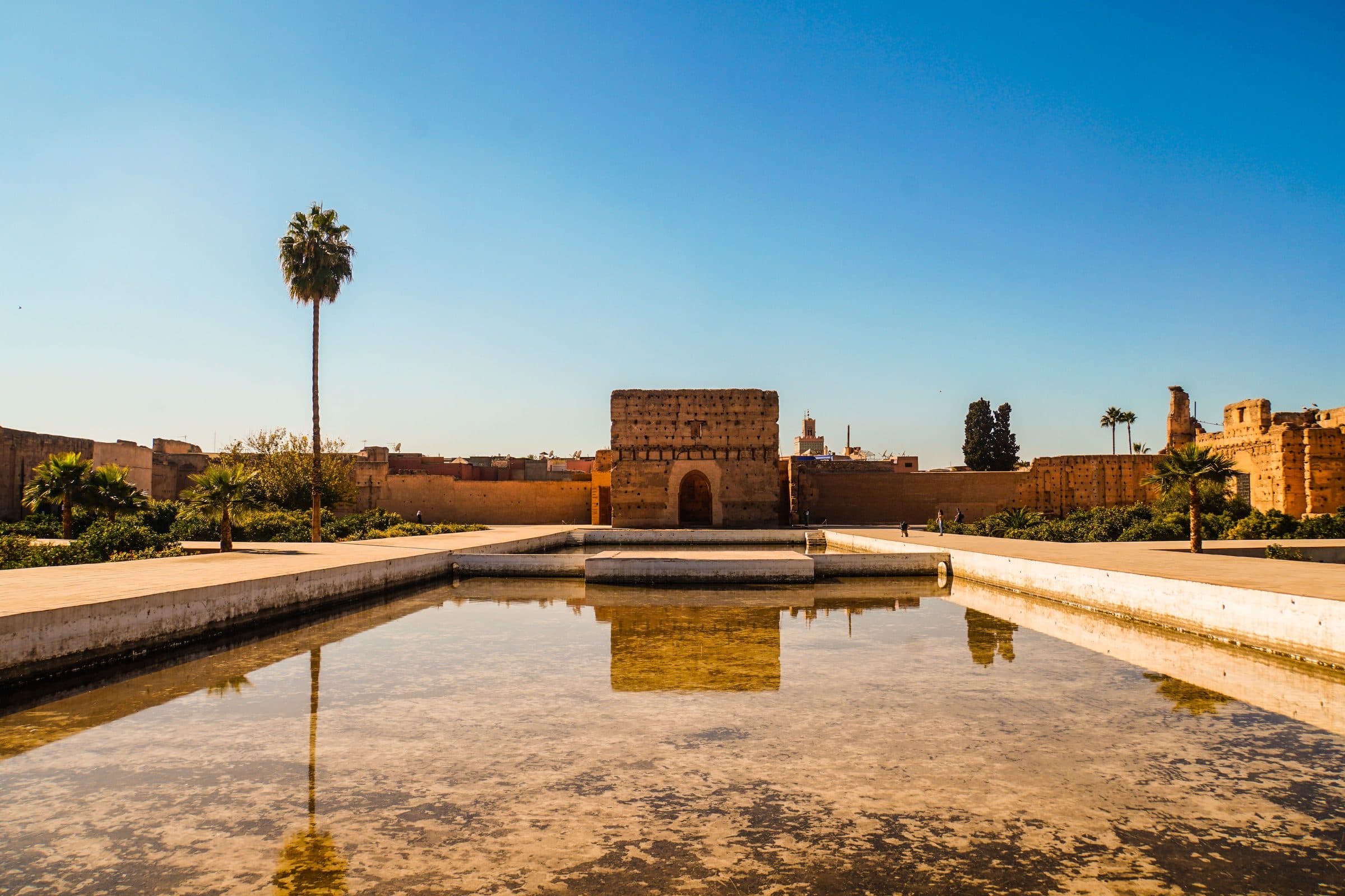 Palácio El Badi em Marrakech sob céu azul com espelho d'água em primeiro plano