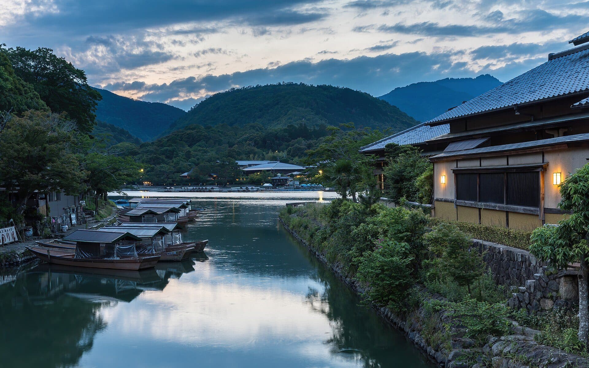 Barcos de passeio na margem do rio Katsura com edifício iluminado ao pôr do sol em Quioto