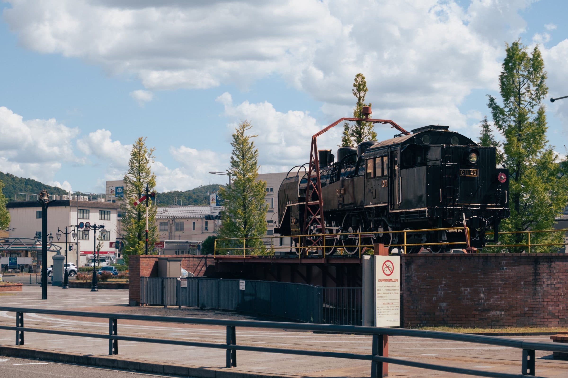 Locomotiva a vapor histórica em exposição em Fukuchiyama, Quioto, com a cidade ao fundo sob céu claro