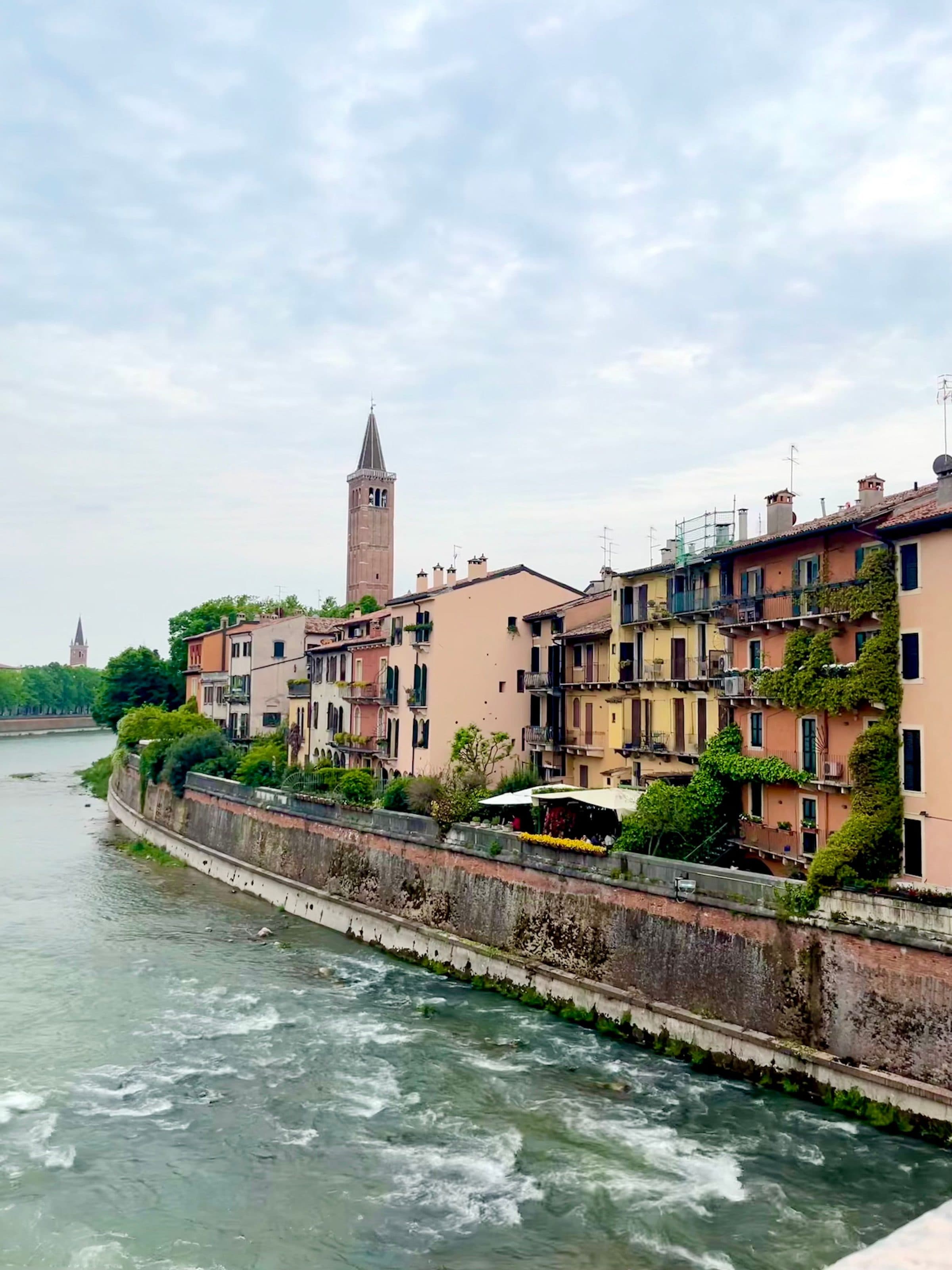 Edifícios coloridos às margens do rio Adige em Verona, Itália, sob céu nublado