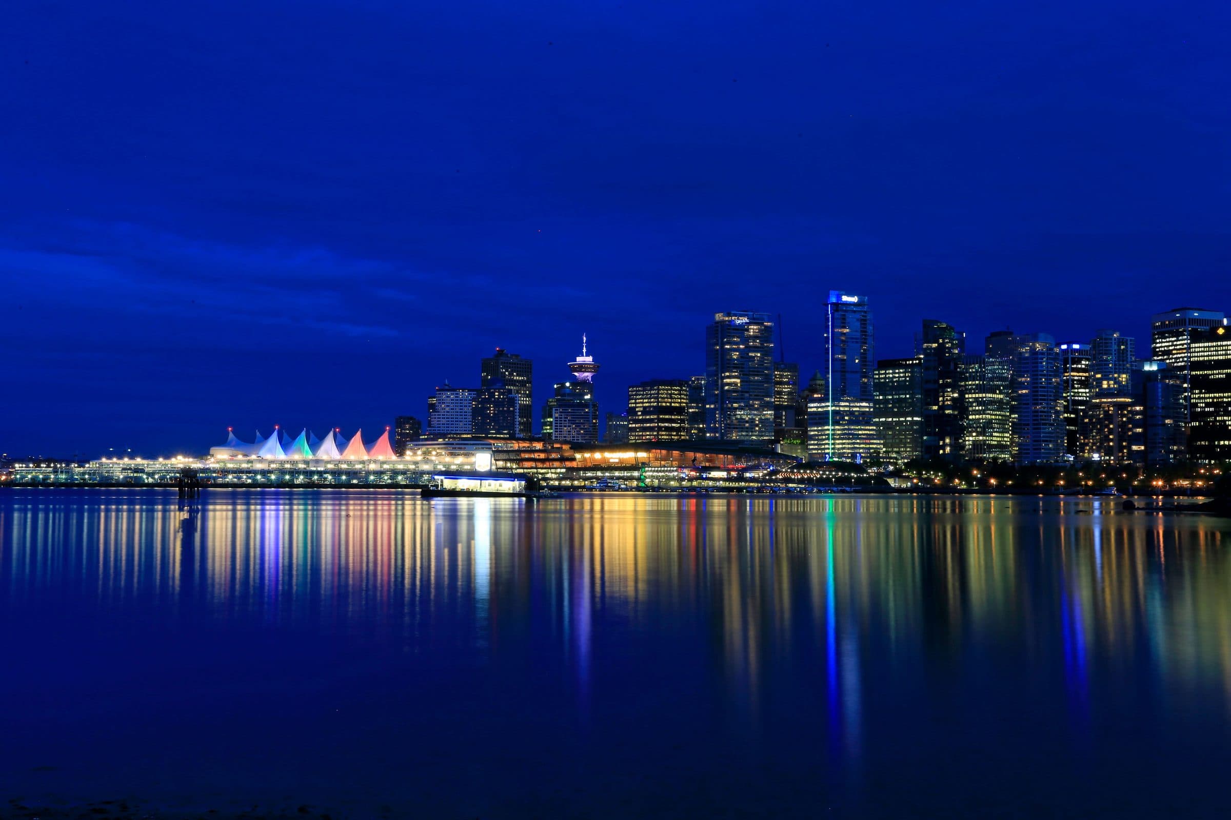 Vista noturna dos prédios iluminados de Vancouver refletidos na água da orla