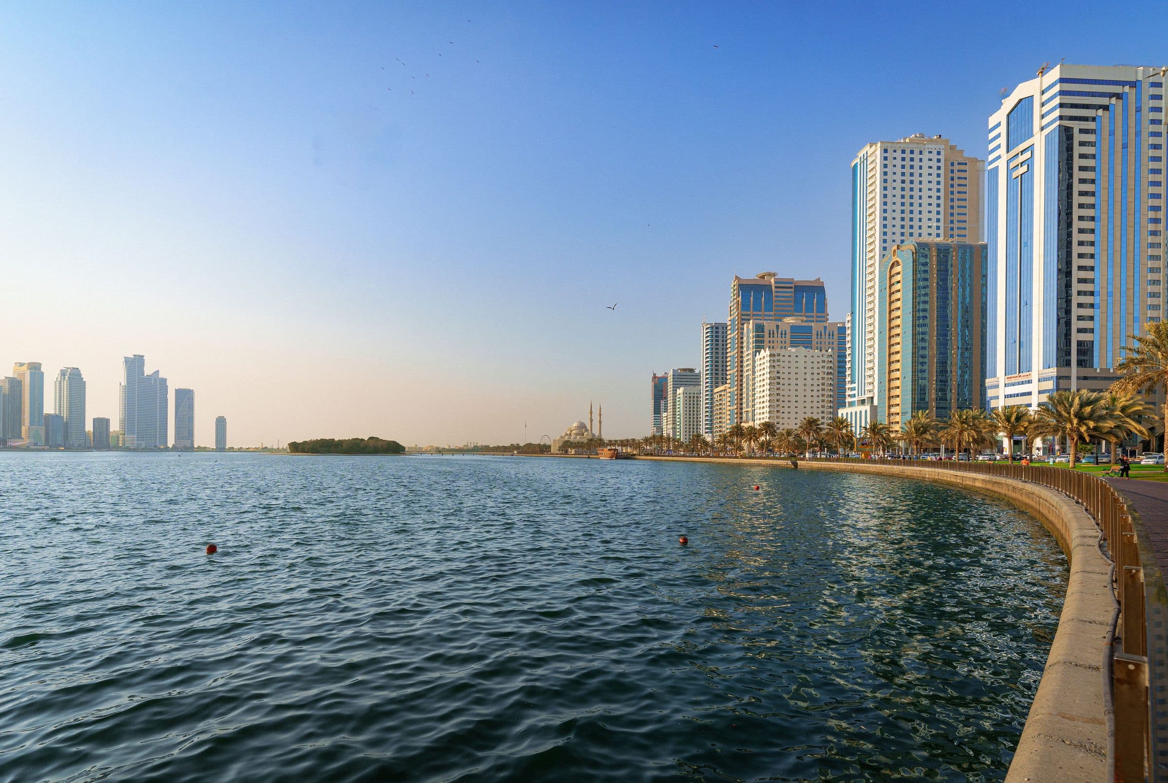 Vista diurna da orla de Sharjah com arranha-céus modernos e águas azuis calmas