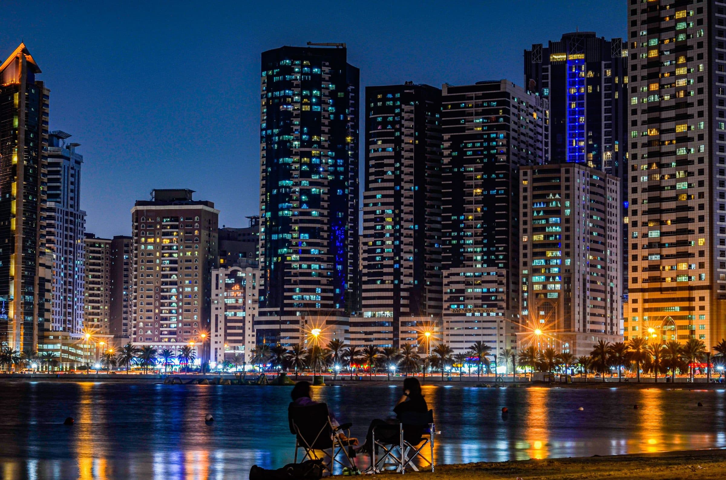 Vista noturna de Sharjah com arranha-céus iluminados e reflexos na água