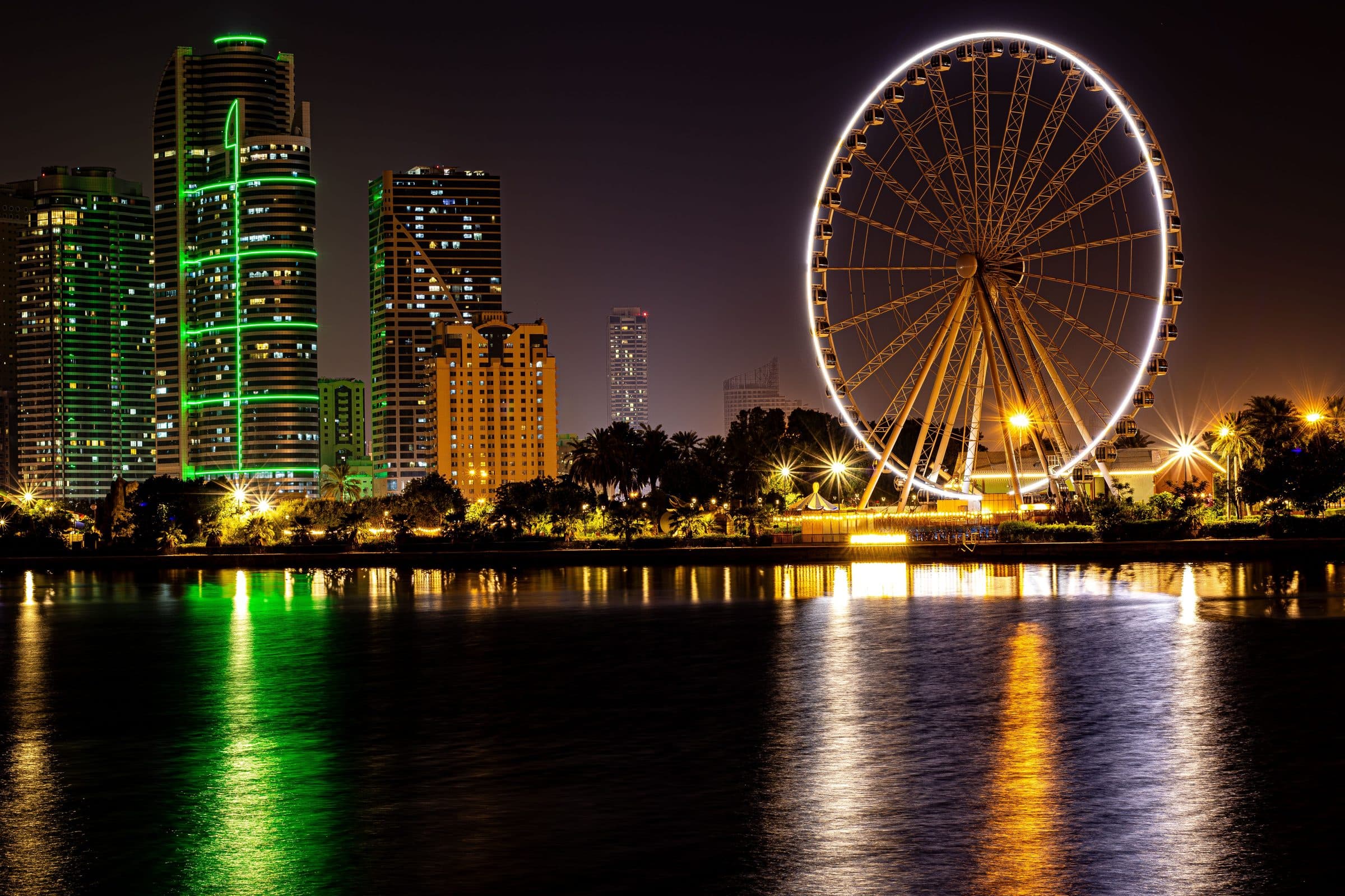 Vista noturna da cidade de Sharjah com uma roda-gigante iluminada refletida na água