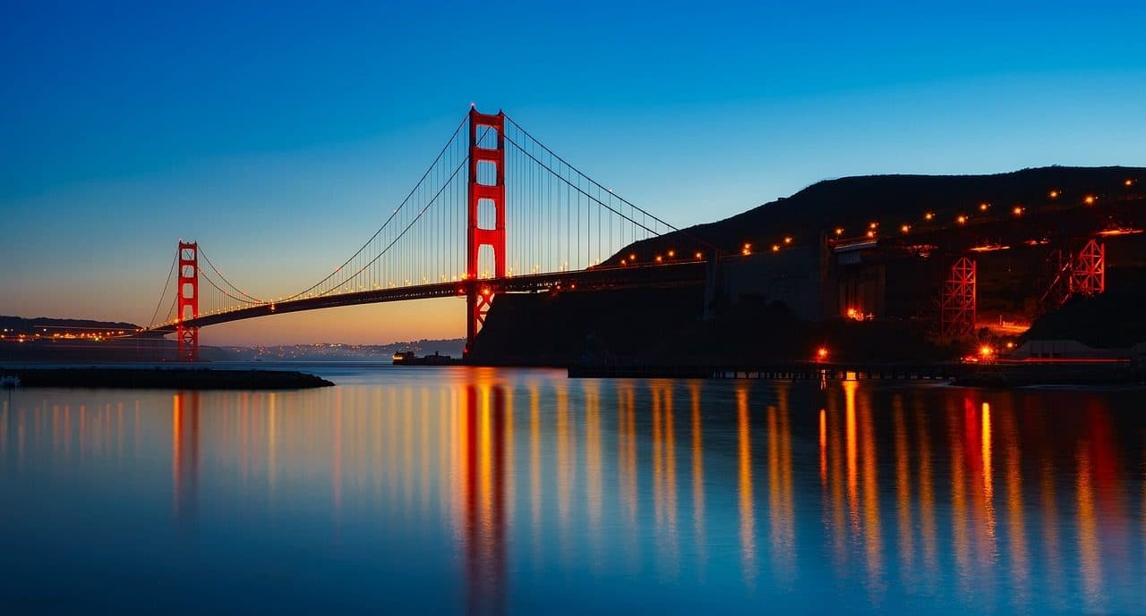 Golden Gate Bridge iluminada ao pôr do sol com reflexo na água da baía de San Francisco