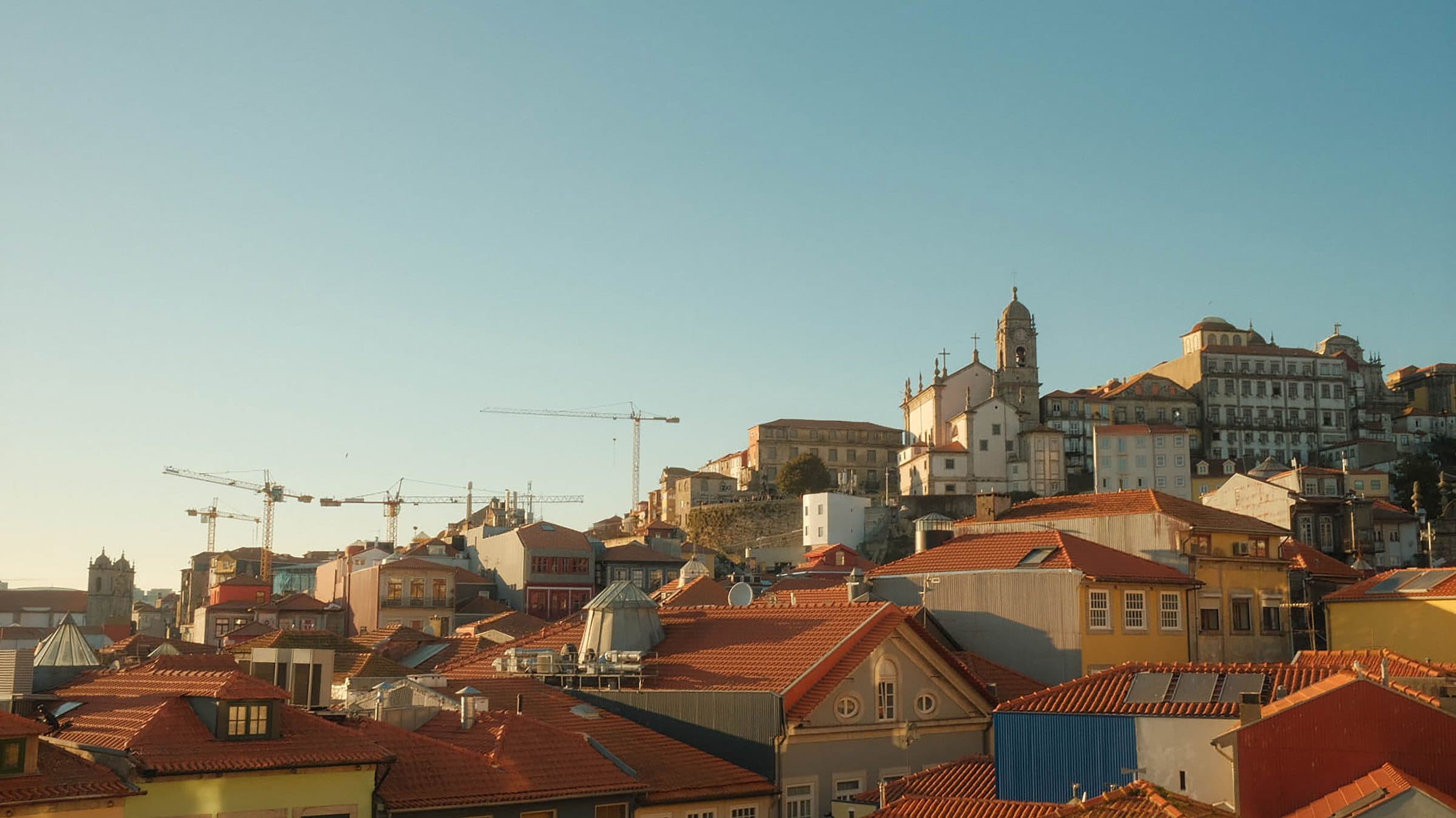Vista panorâmica de Porto, Portugal, com telhados históricos e guindastes ao pôr do sol