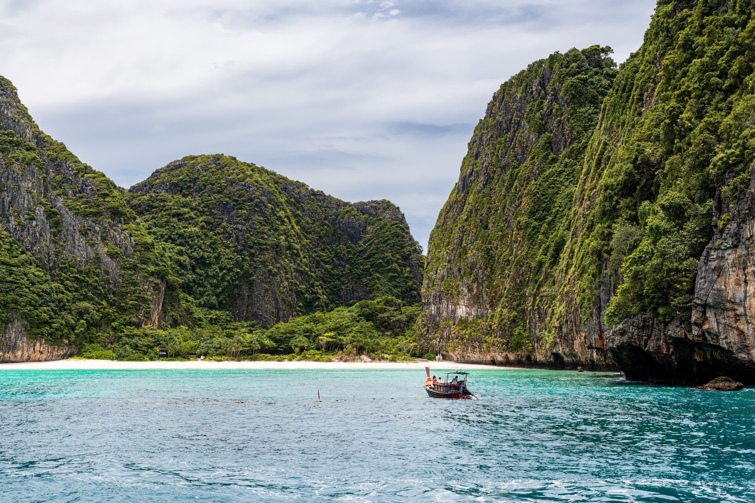 Barco tradicional em águas azul-turquesa próximo a falésias de calcário em Phuket, Tailândia