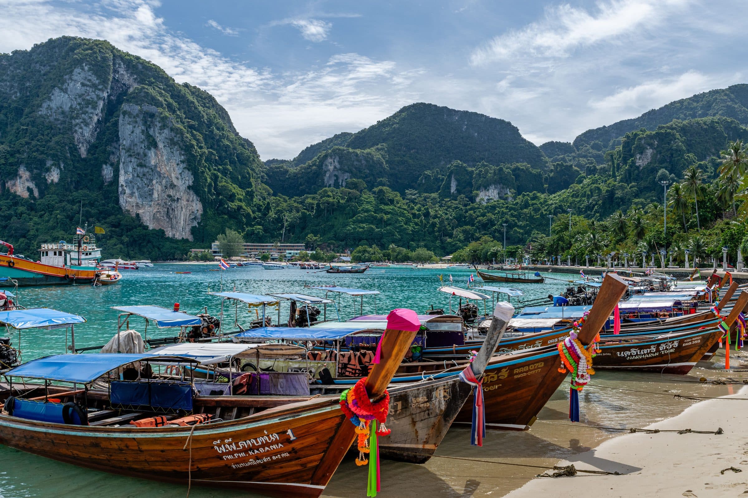 Barcos longtail alinhados em uma praia de Phuket, na Tailândia, com montanhas verdes ao fundo