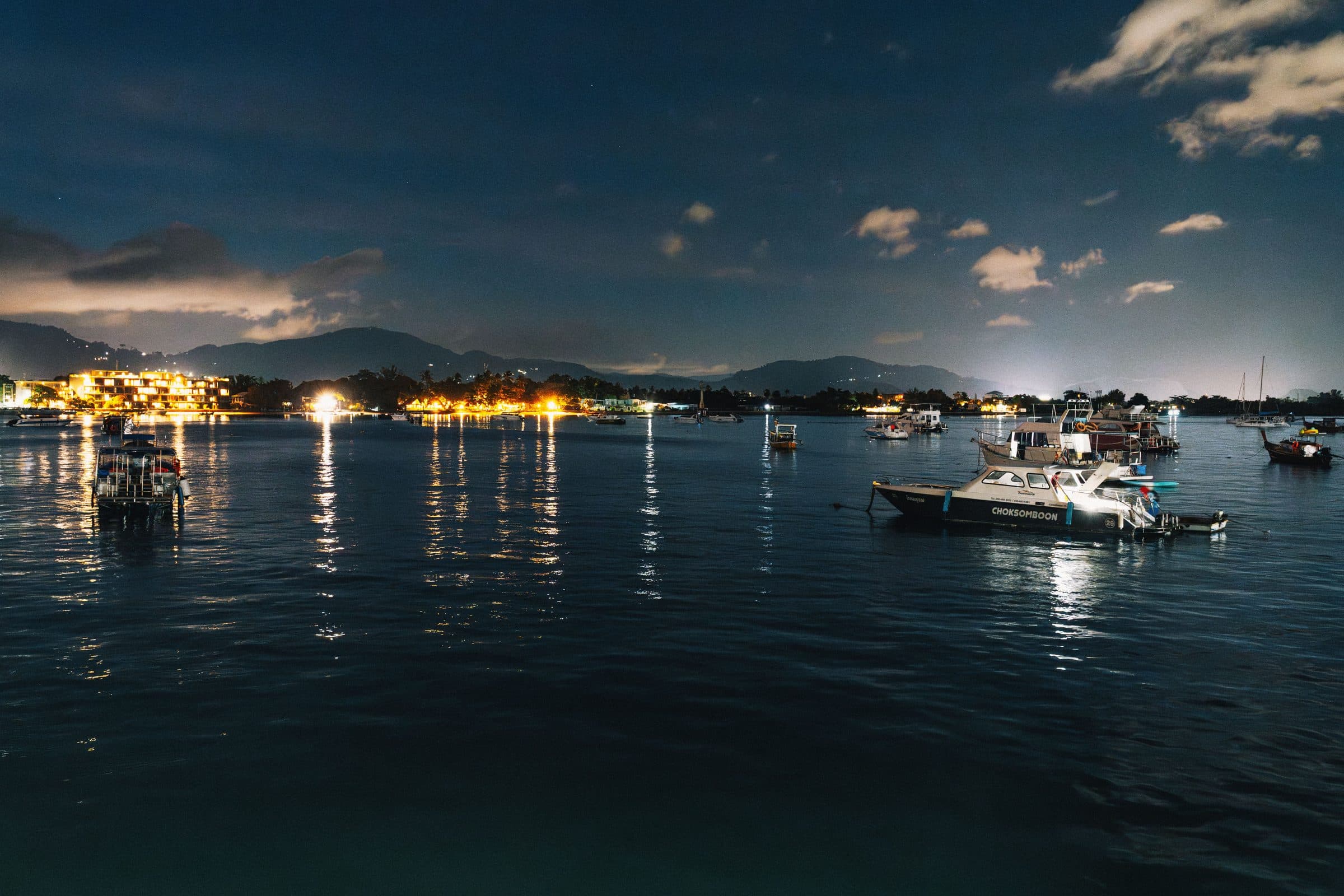 Barcos refletidos na água de um porto à noite sob céu estrelado em Phuket