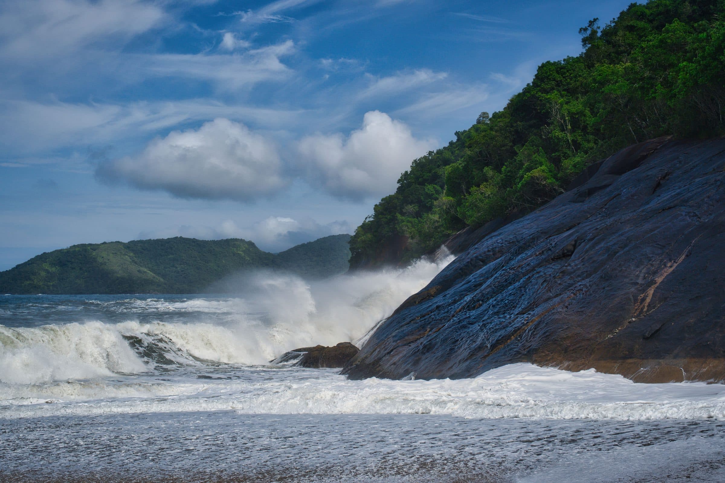 Ondas quebrando contra a costa rochosa sob céu azul em Ubatuba