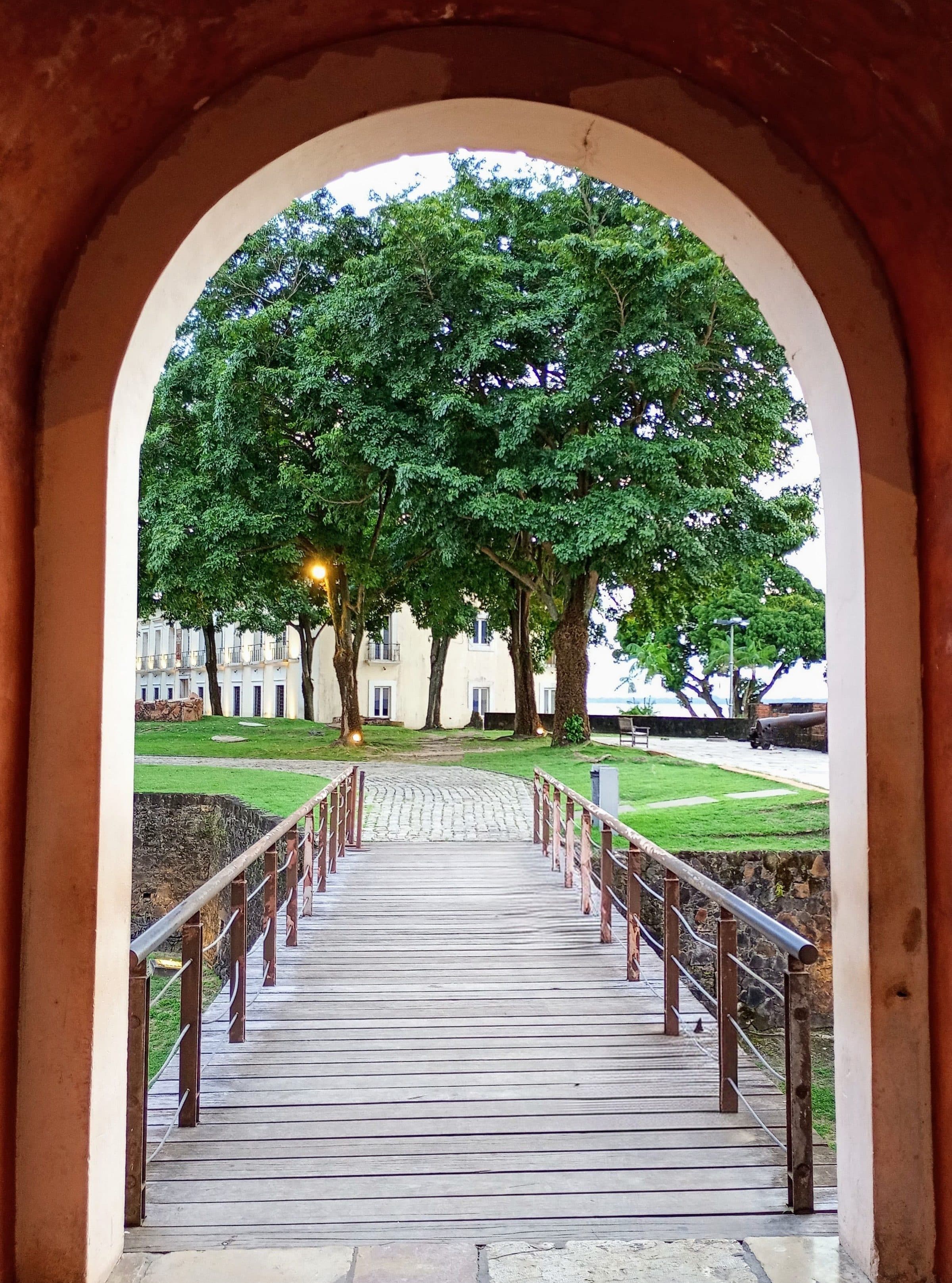 Ponte de madeira e árvores verdes vistas através de um arco em Belém