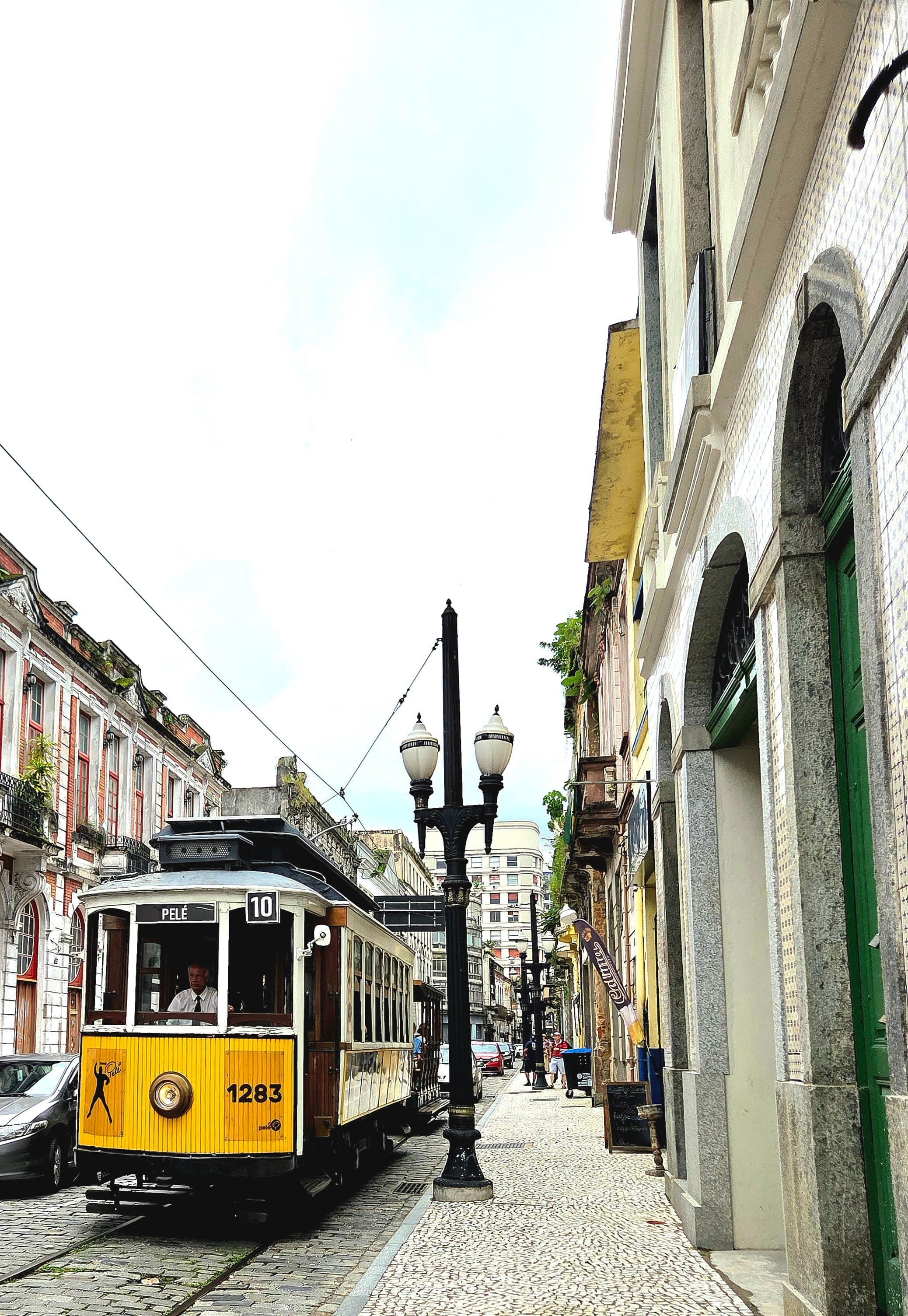 Bonde amarelo antigo percorre rua de paralelepípedos entre edifícios históricos em Santos