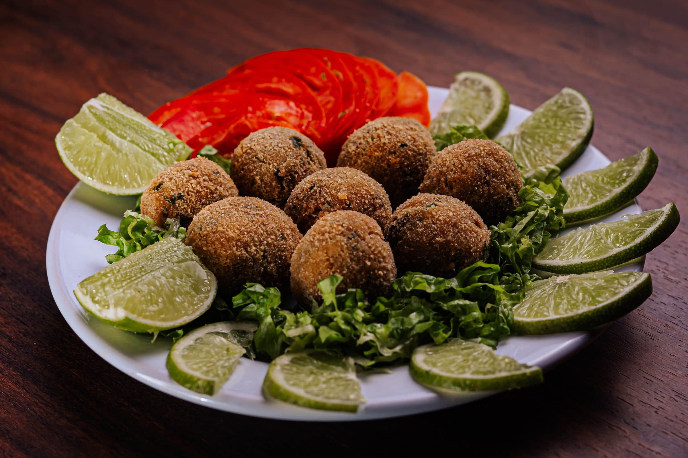 Bolinhos de falafel acompanhados de limão e vegetais sobre uma mesa de madeira