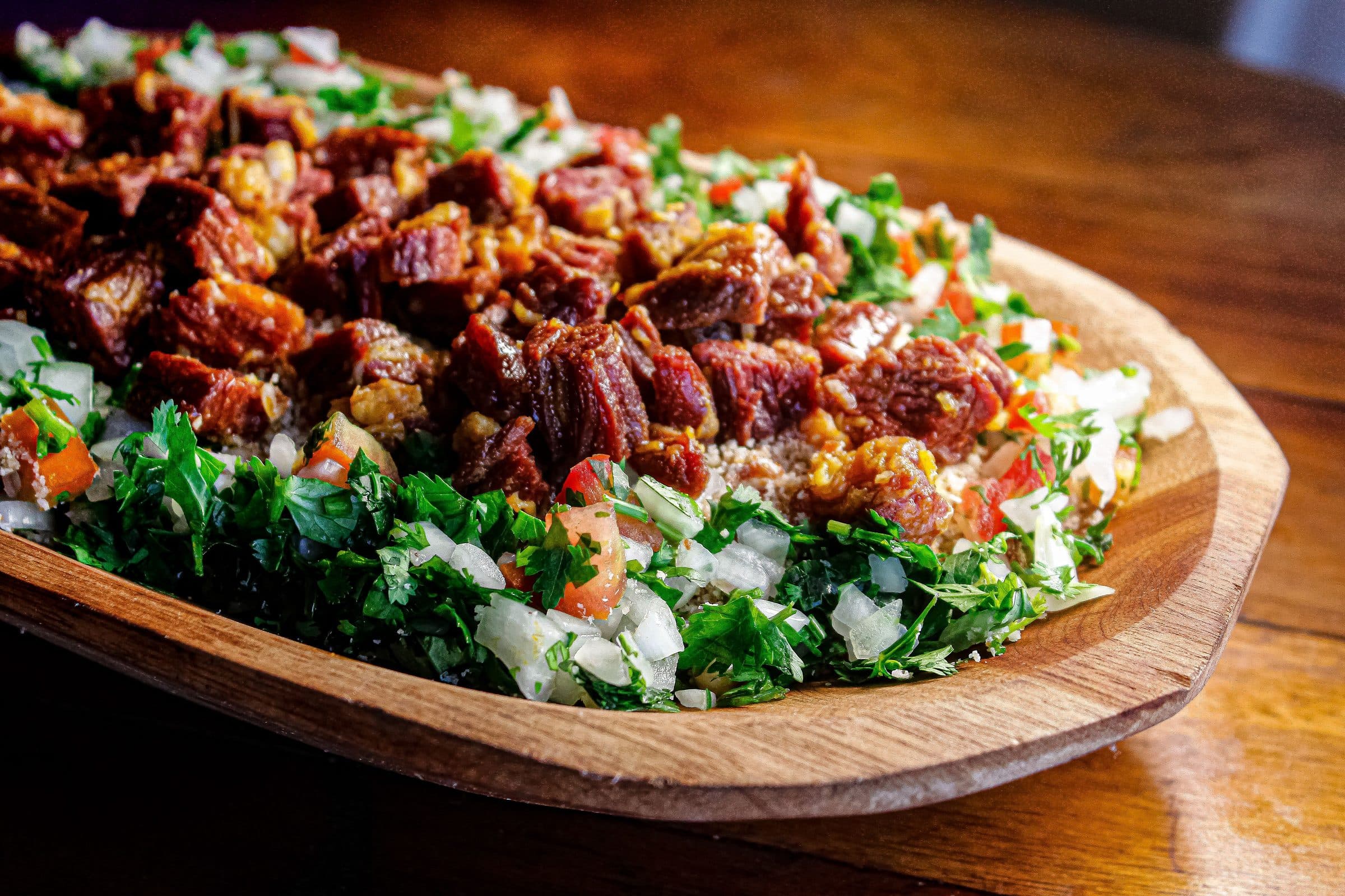 Carne de sol servida com ervas e legumes frescos em uma tábua de madeira