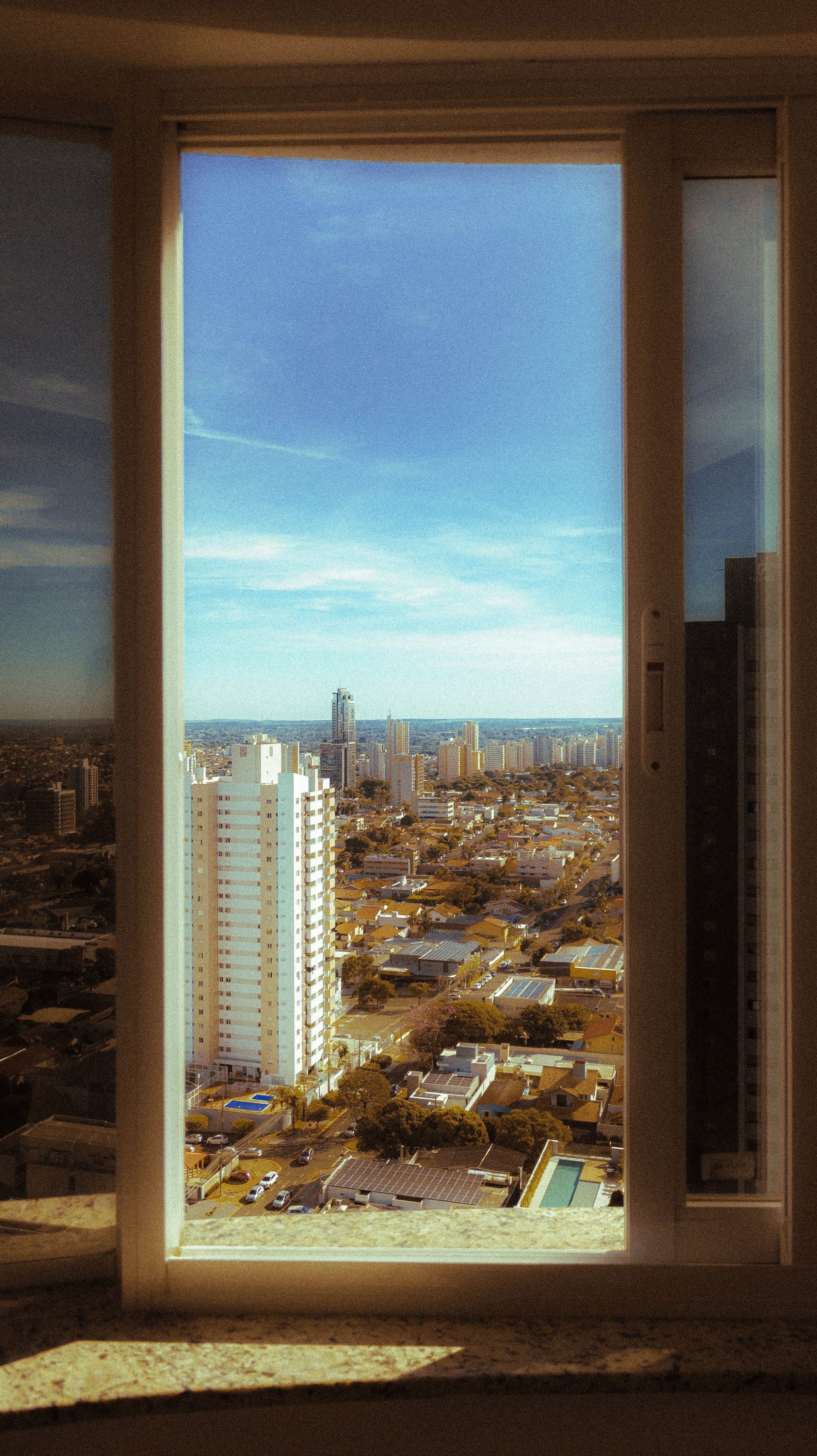 Vista da cidade de Campo Grande pela janela de um apartamento com céu azul