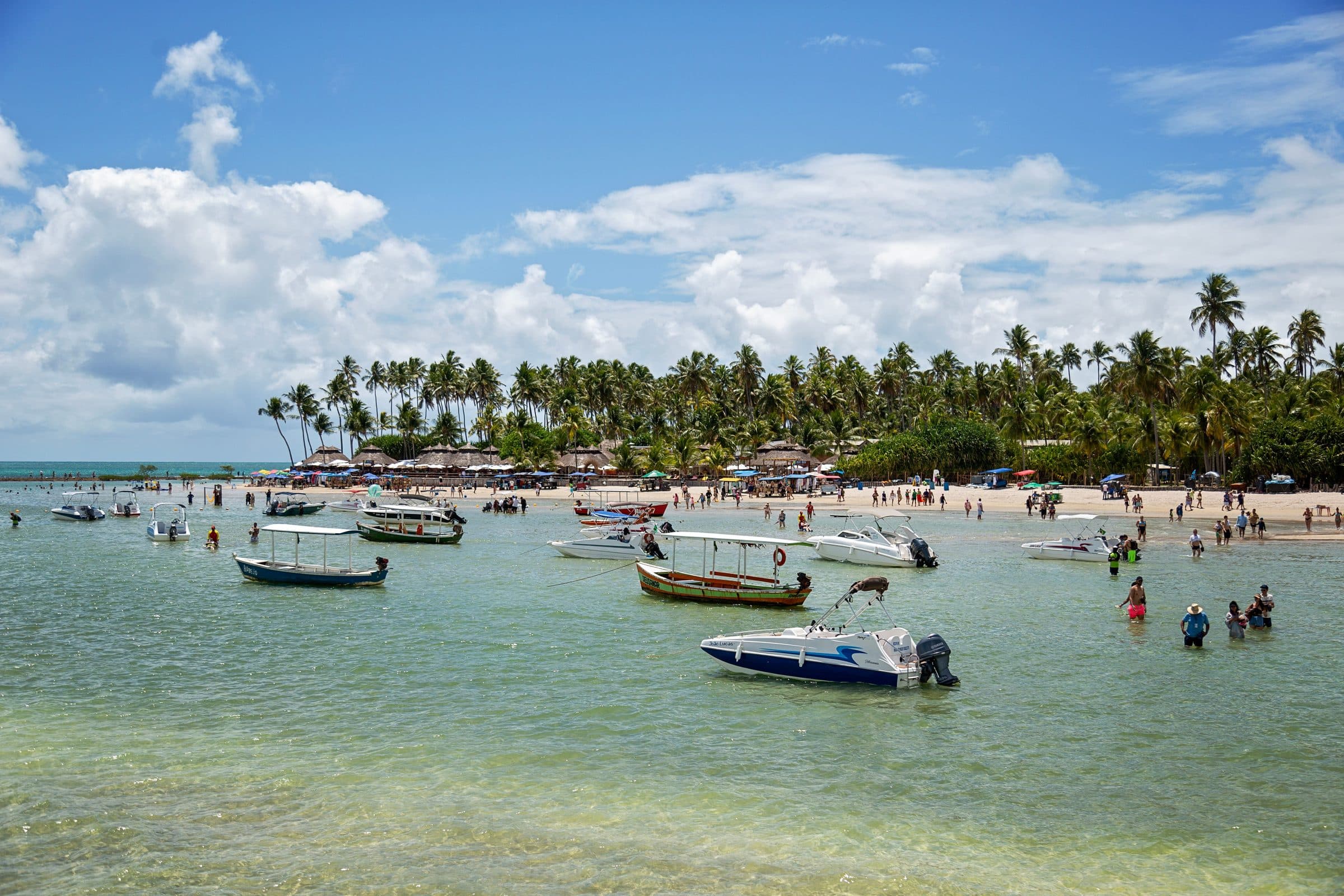 Praia tropical com barcos e turistas sob céu azul