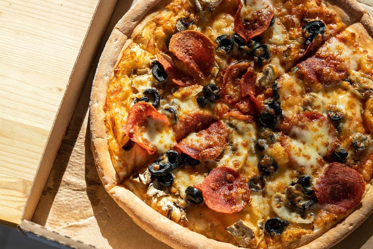 Pizza de pepperoni com cogumelos e azeitonas pretas dentro de uma caixa aberta