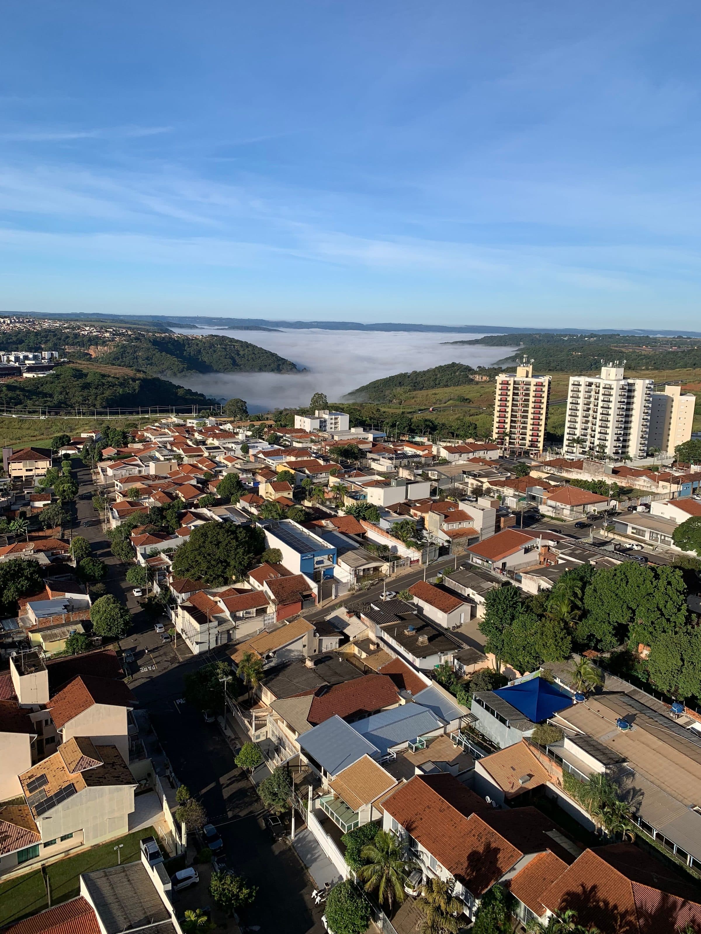 Vista aérea da cidade de Bauru com névoa matinal sobre colinas ao fundo e céu claro