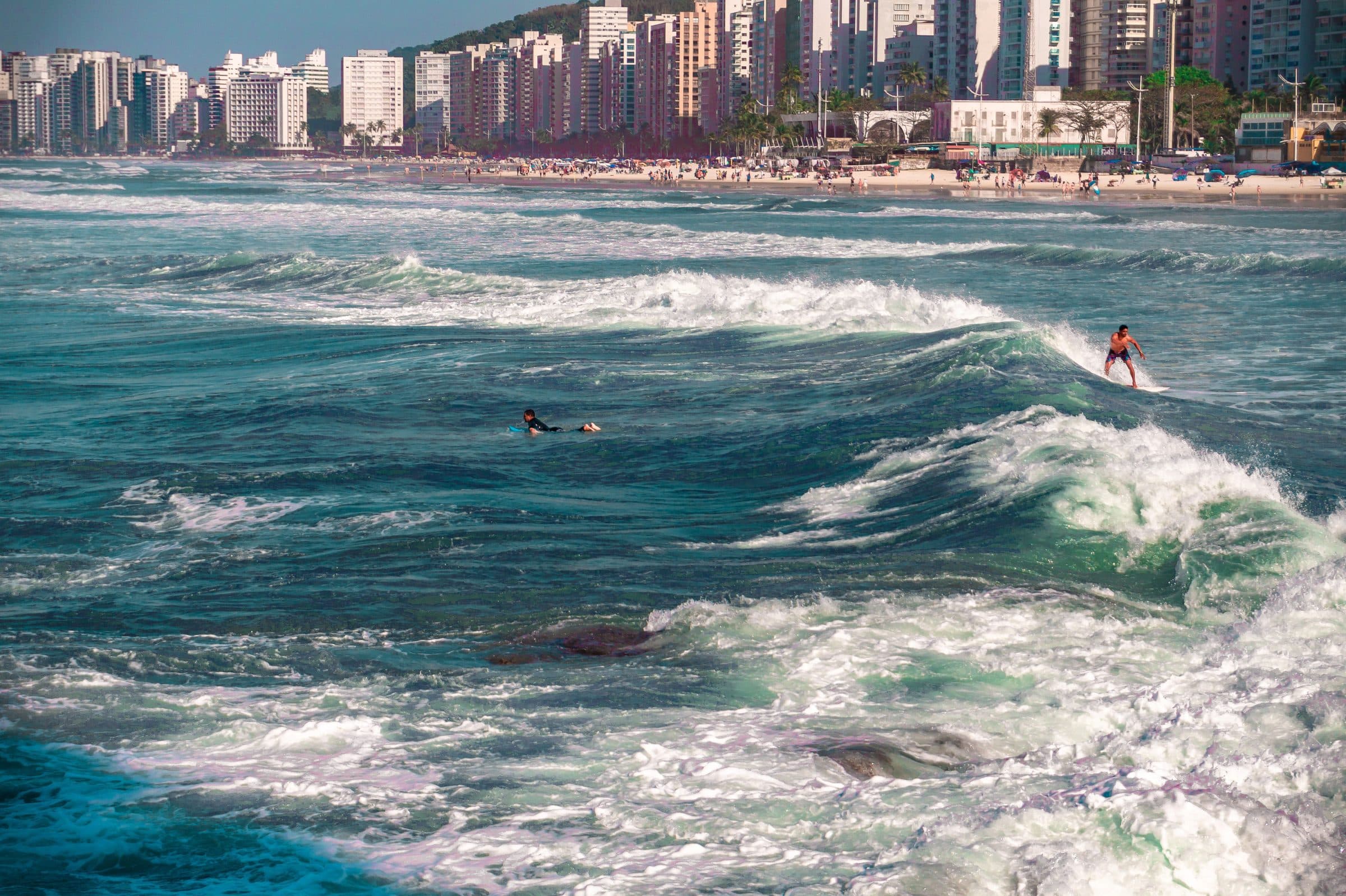 Pessoa surfando nas ondas da praia de Bertioga com a orla urbana ao fundo