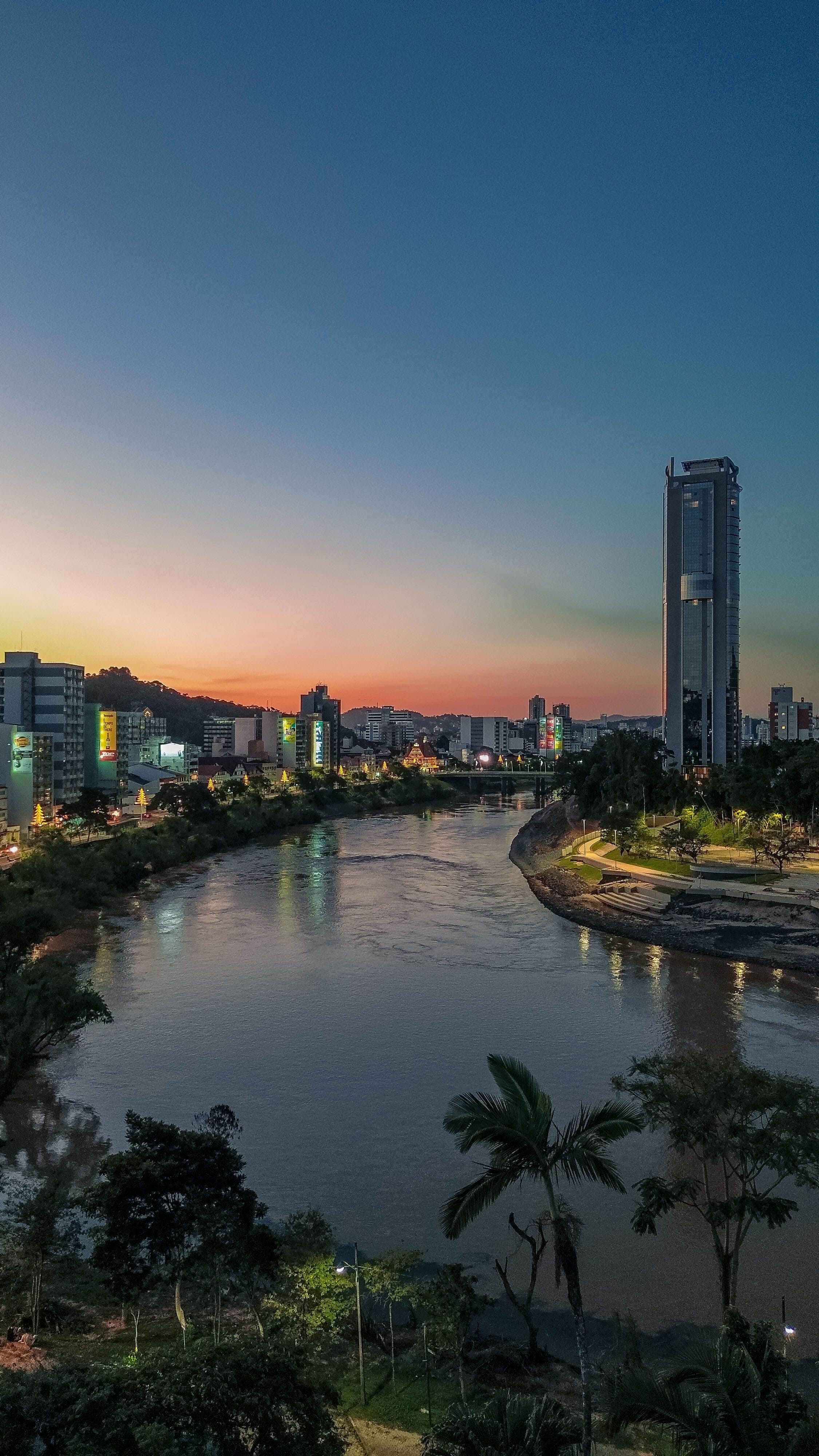 Vista de Blumenau ao pôr do sol com rio cercado por edifícios modernos
