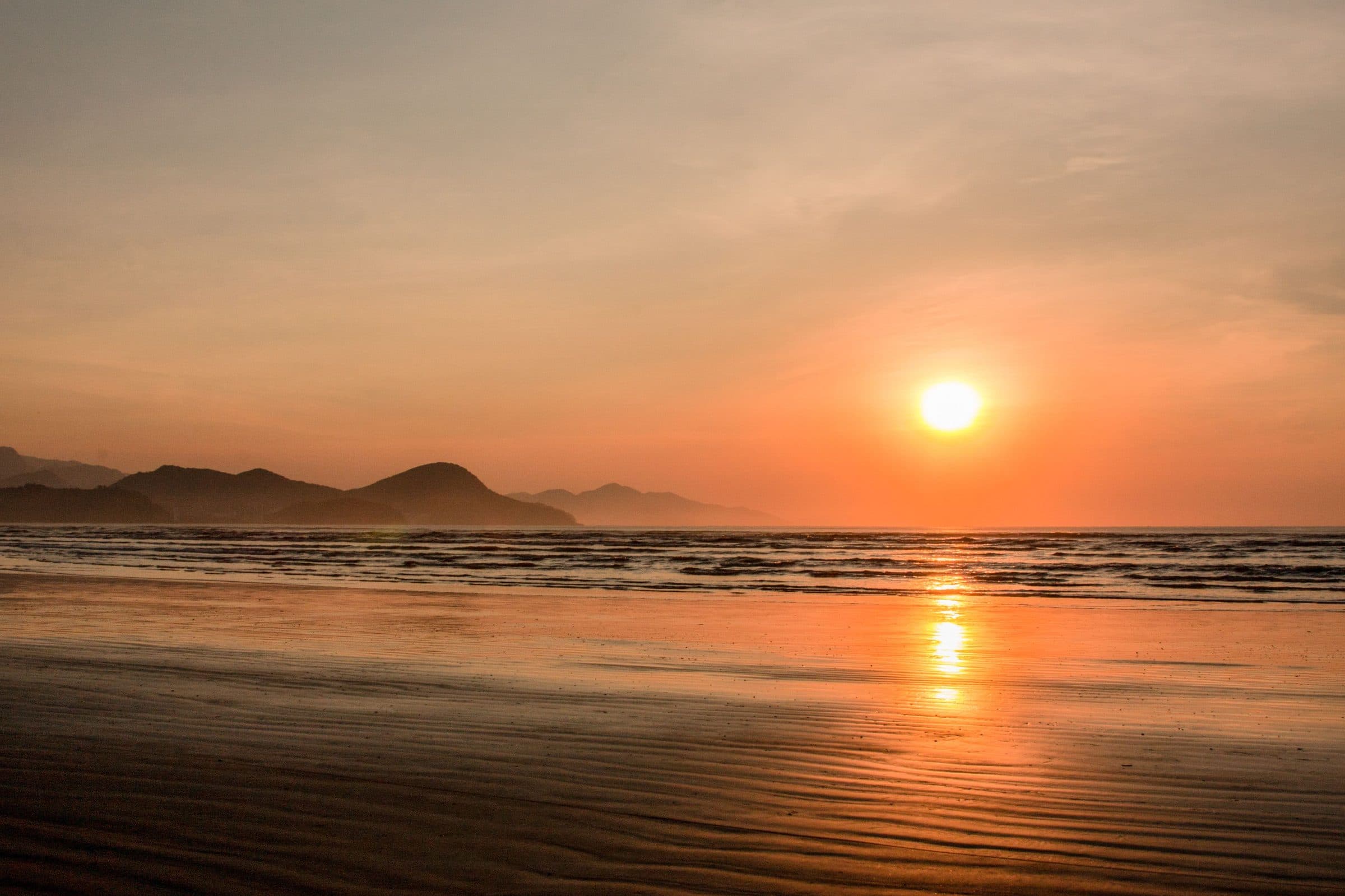 Pôr do sol na praia de Caraguatatuba com ondas calmas e horizonte colorido