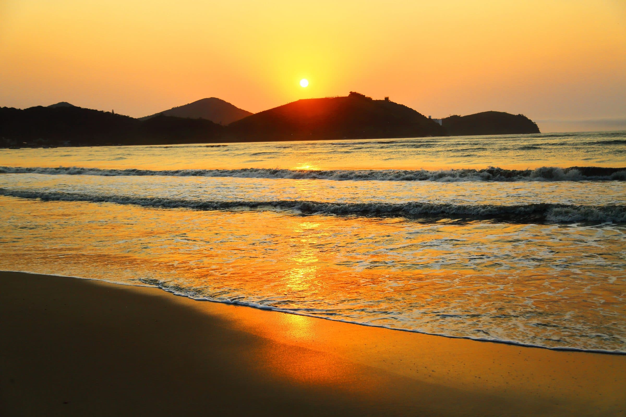 Pôr do sol na praia de Caraguatatuba com ondas no mar e horizonte dourado