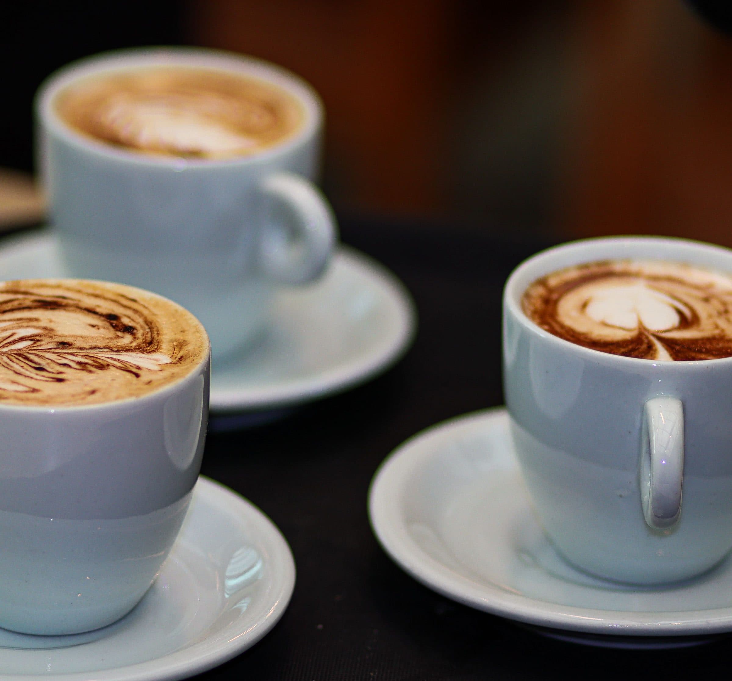 Três xícaras brancas com cappuccinos decorados com latte art sobre pires