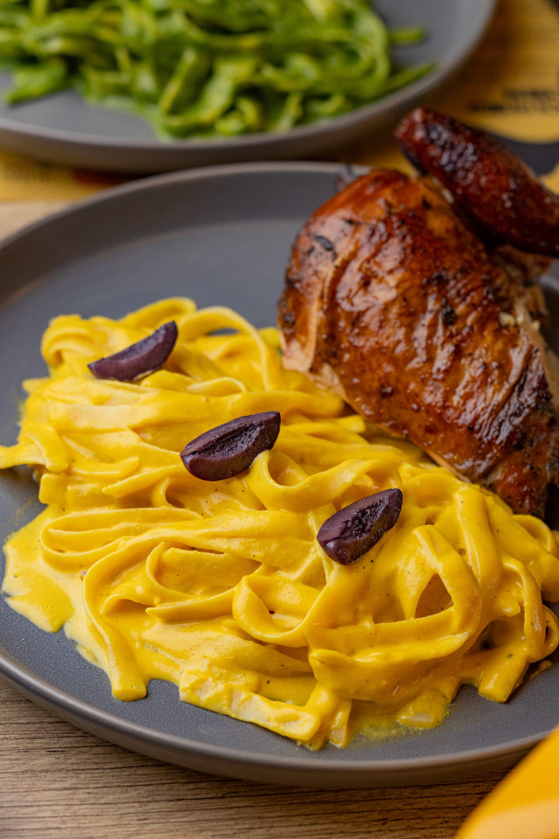 Prato com massa cremosa ao molho huancaína, coxa de frango assada e azeitonas