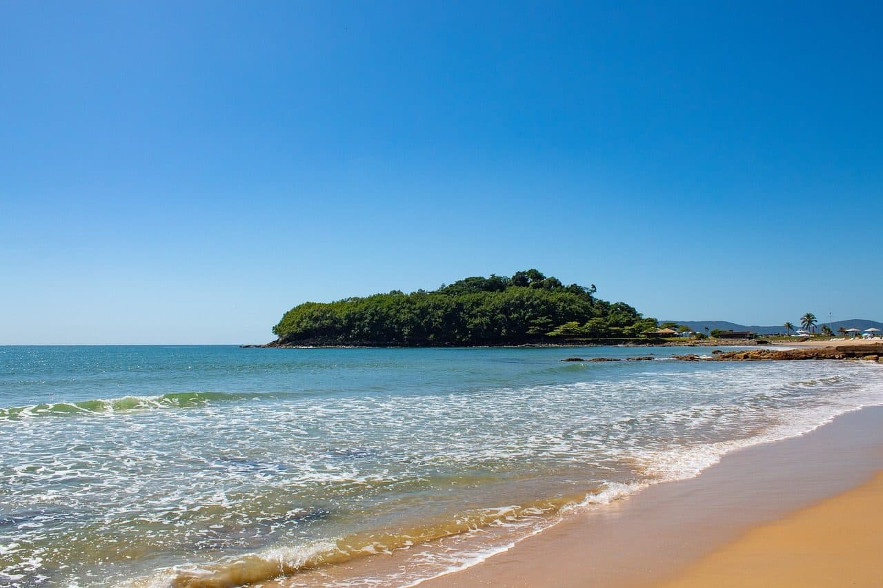 Faixa de areia e mar com ondas sob céu azul na praia de Itapema, Santa Catarina