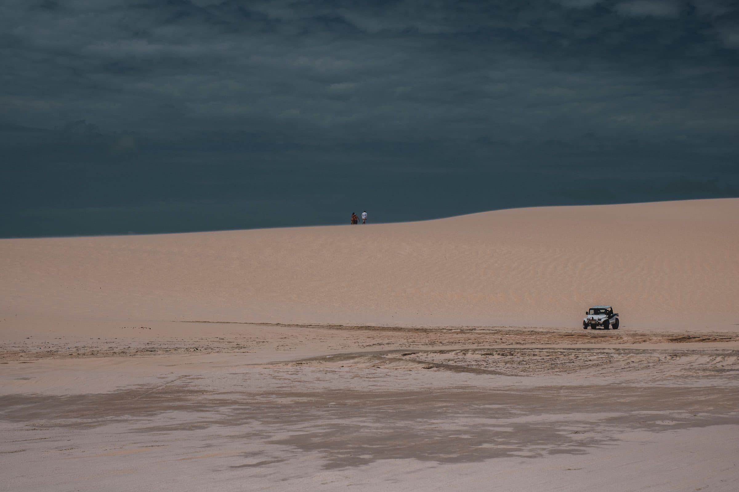 Jeep percorrendo as dunas de areia de Jericoacoara sob céu nublado
