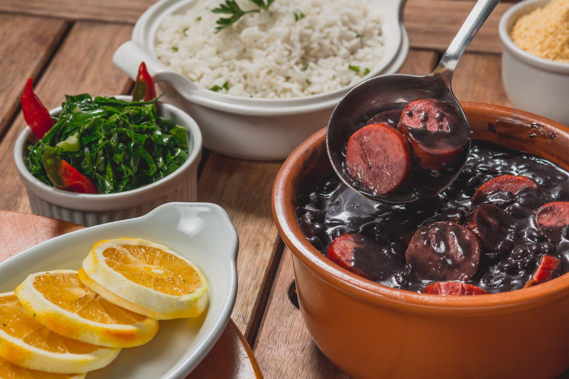 Feijoada servida com arroz, couve e fatias de laranja em uma mesa de madeira
