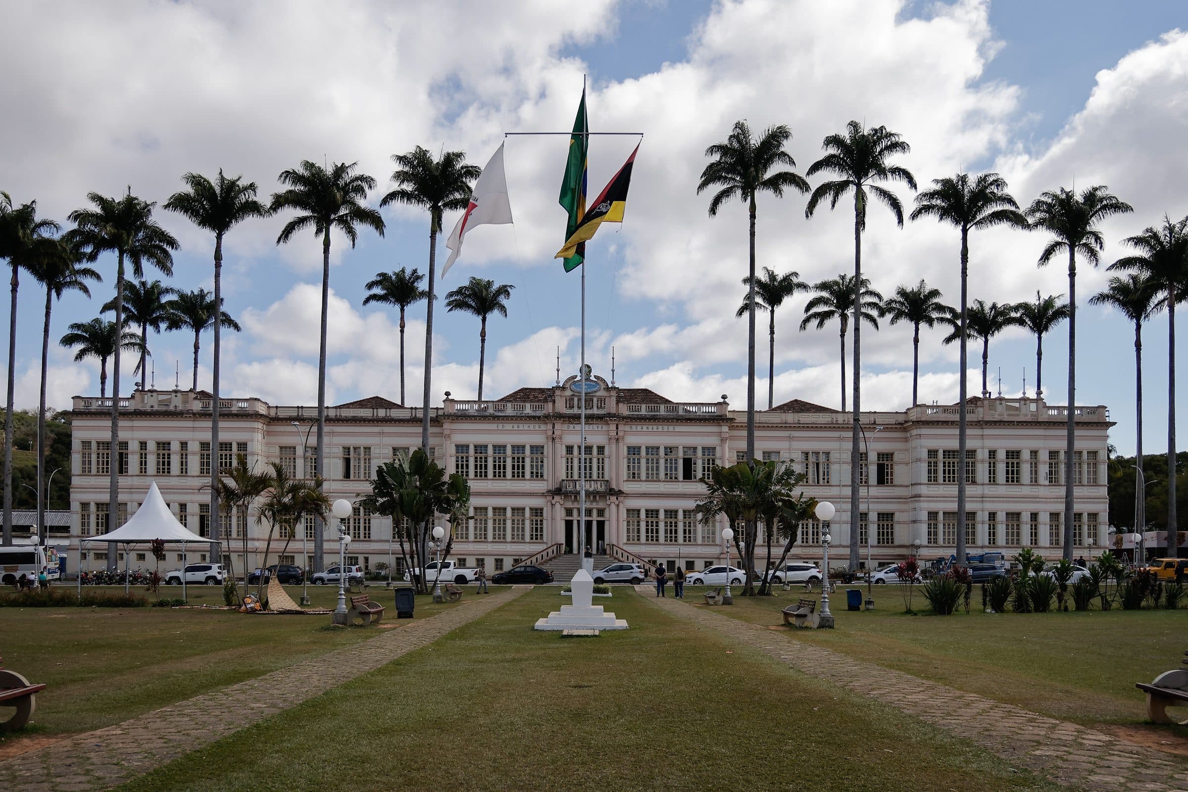 Prédio municipal em Juiz de Fora cercado por palmeiras sob um céu nublado