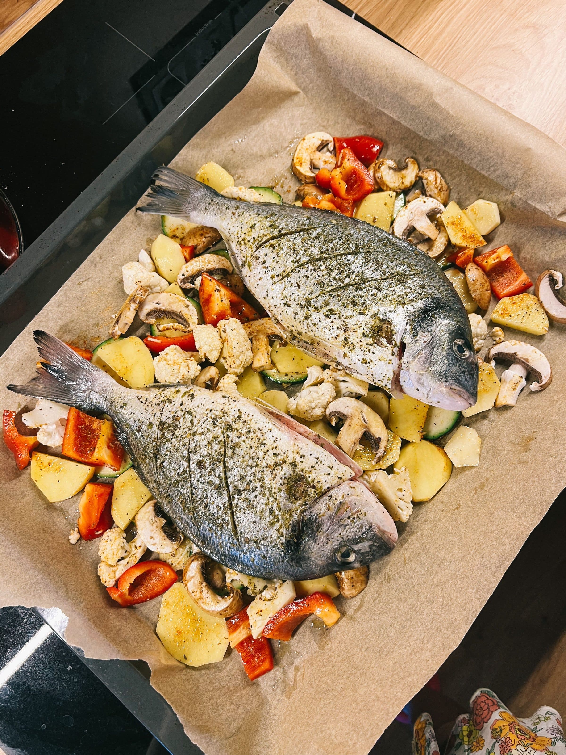 Peixe dourado fresco com legumes fatiados em uma assadeira com papel-manteiga