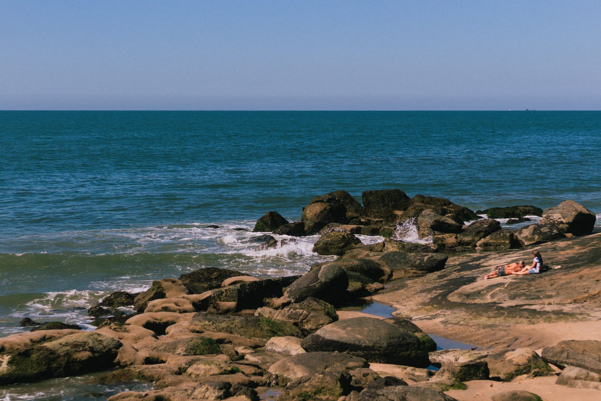 Praia em Matinhos, Paraná, com ondas do mar quebrando na costa rochosa