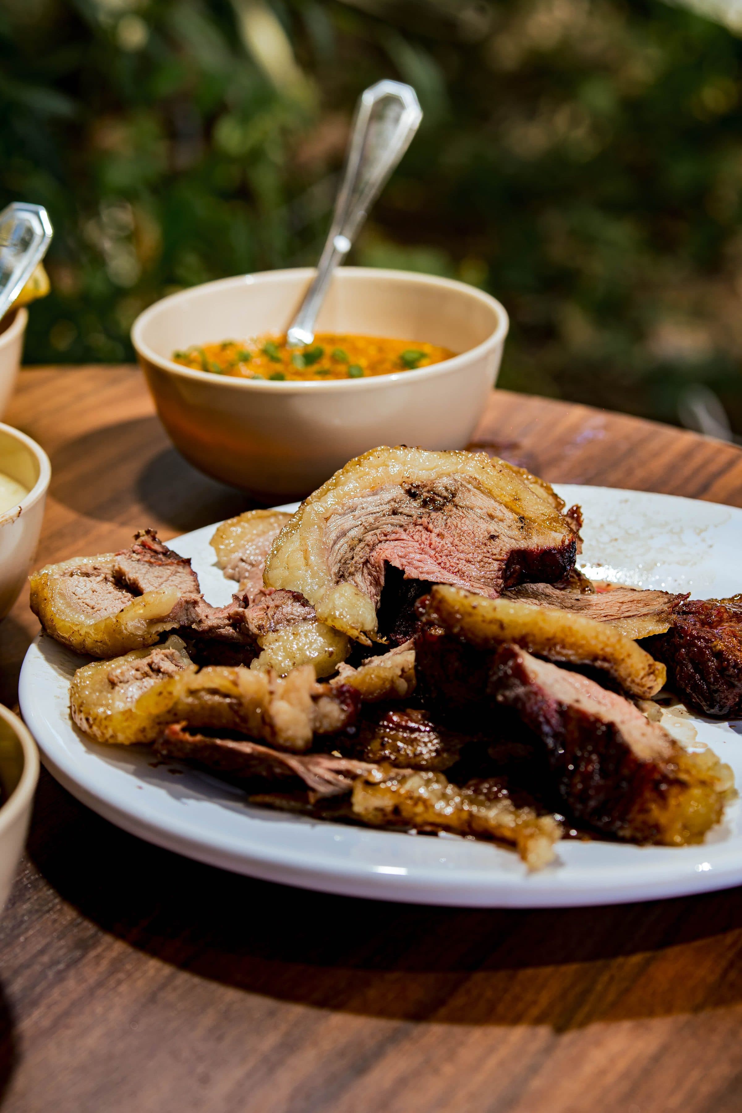 Fatias de carne grelhada servidas em um prato com molho em ambiente rústico ao ar livre