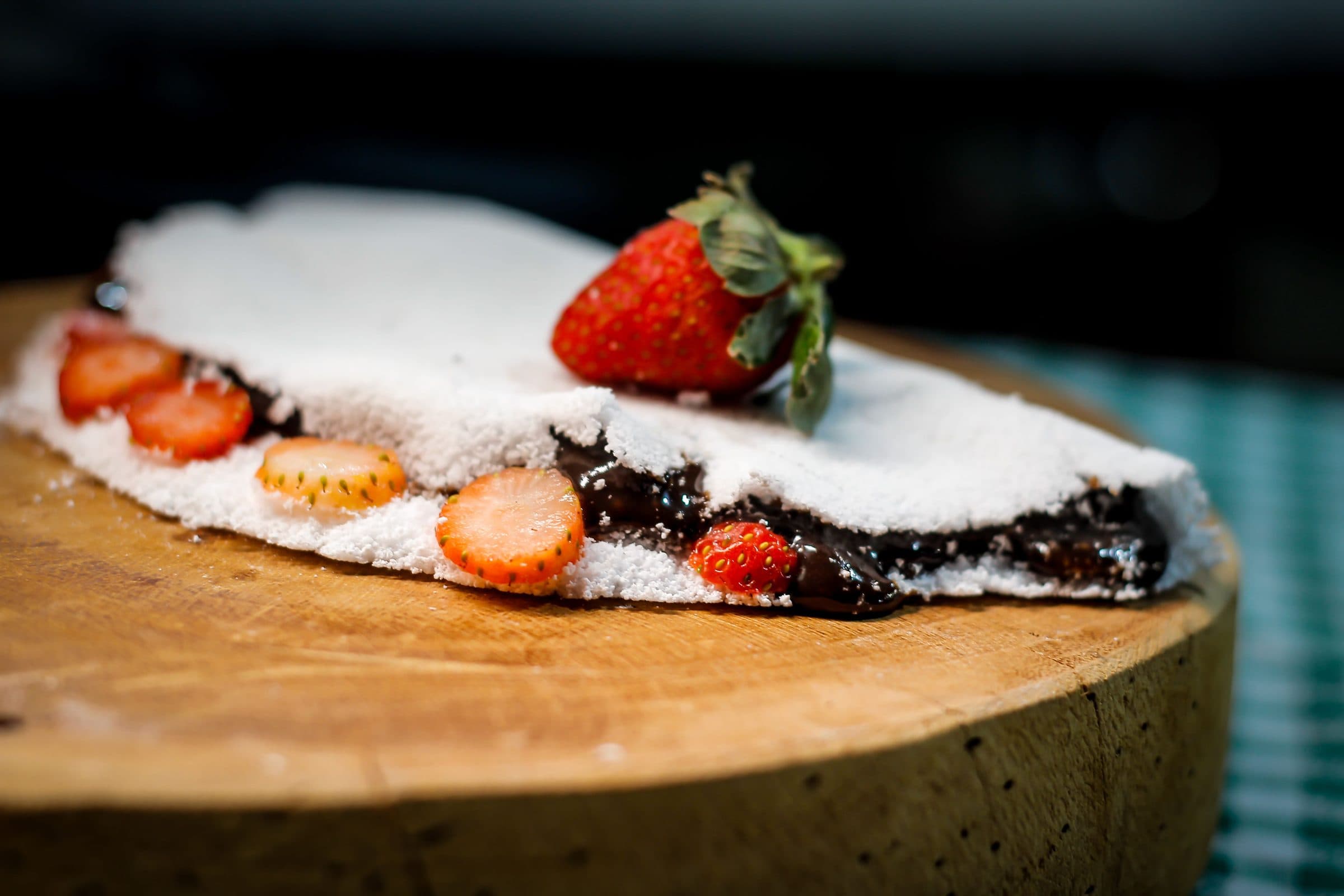 Tapioca recheada com chocolate e morangos sobre tábua de madeira